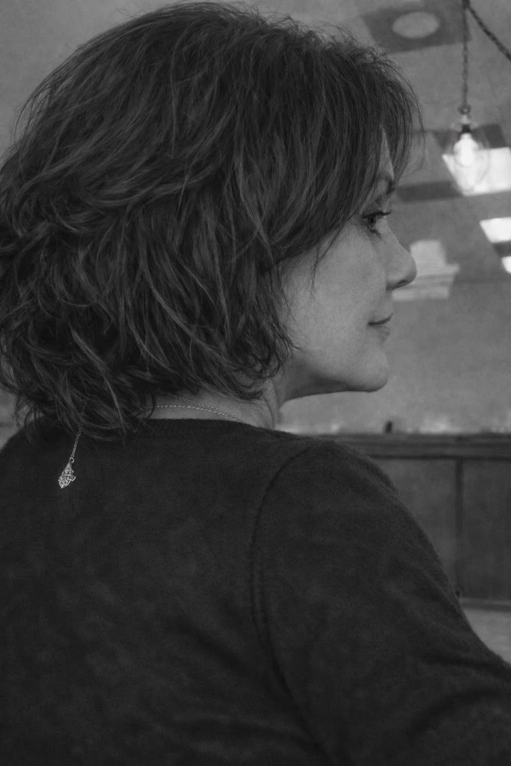 Side profile of a woman with wavy hair, wearing a necklace, in a black and white photo.