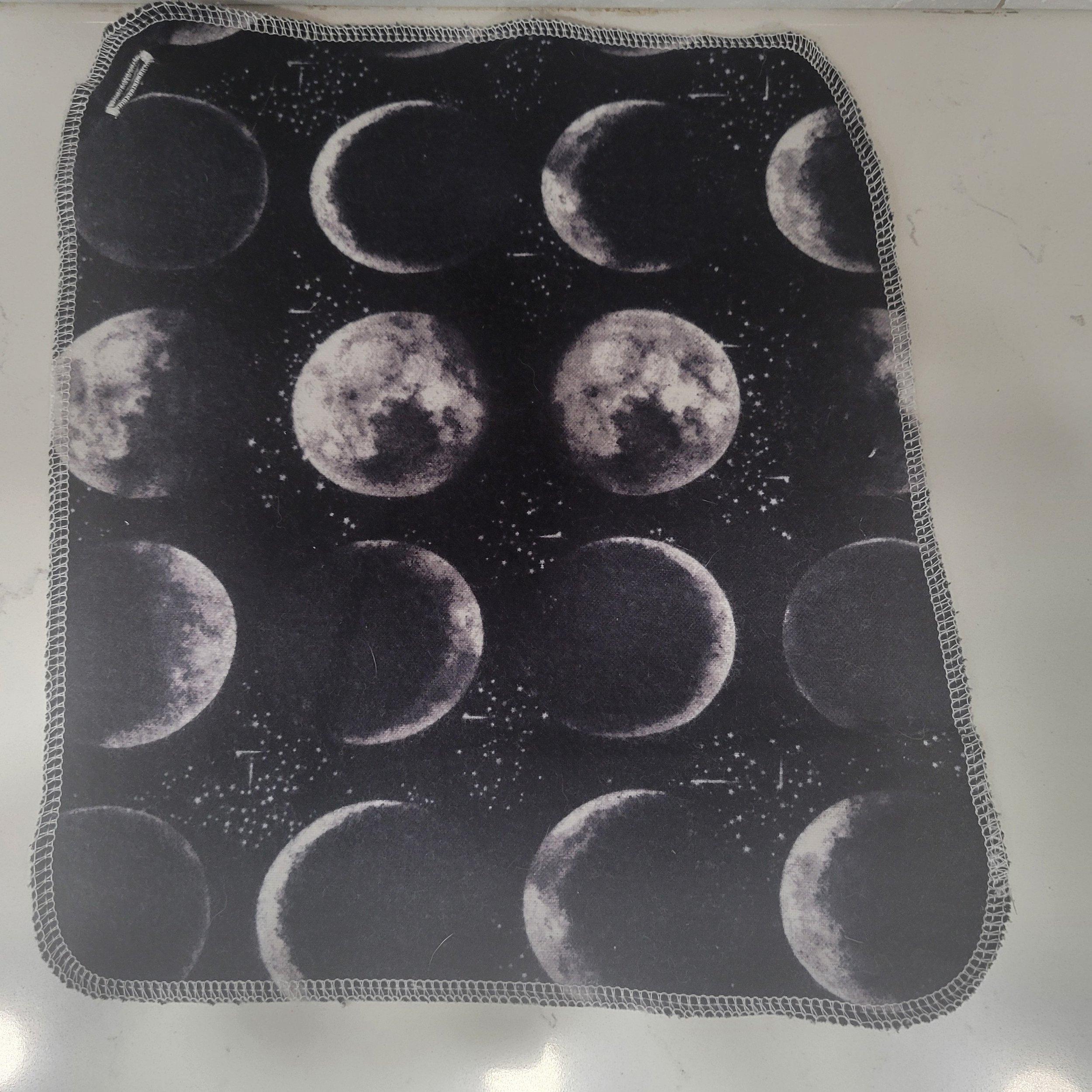 Reusable flannel cloth showing phases of the moon on a black background. Each Go Wipe has a sewn buttonhole for attachment to the included carabiner belt clip