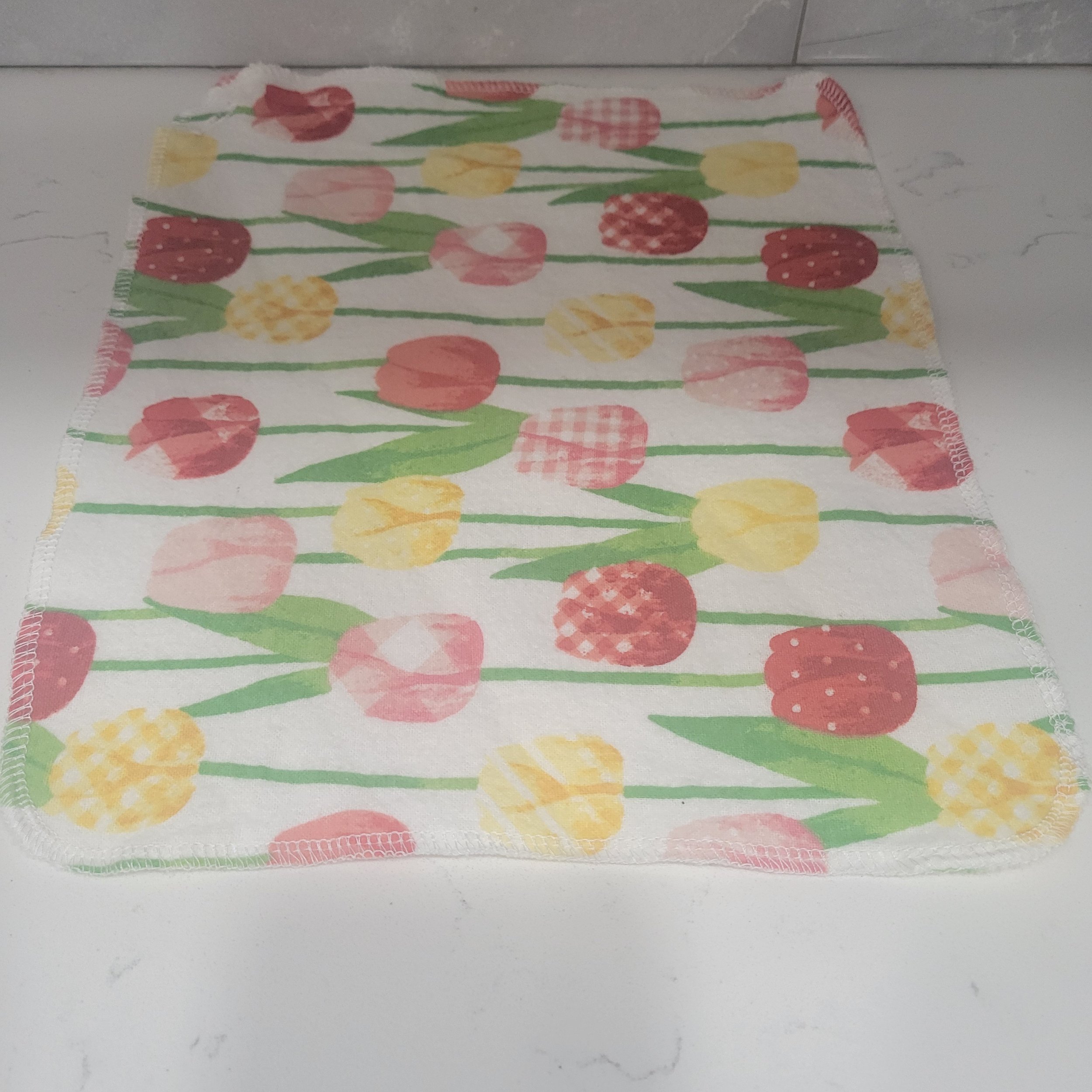 Reusable flannel cloth showing red, yellow and pink tulips on a white background. Each Go Wipe has a sewn buttonhole for attachment to the included carabiner belt clip