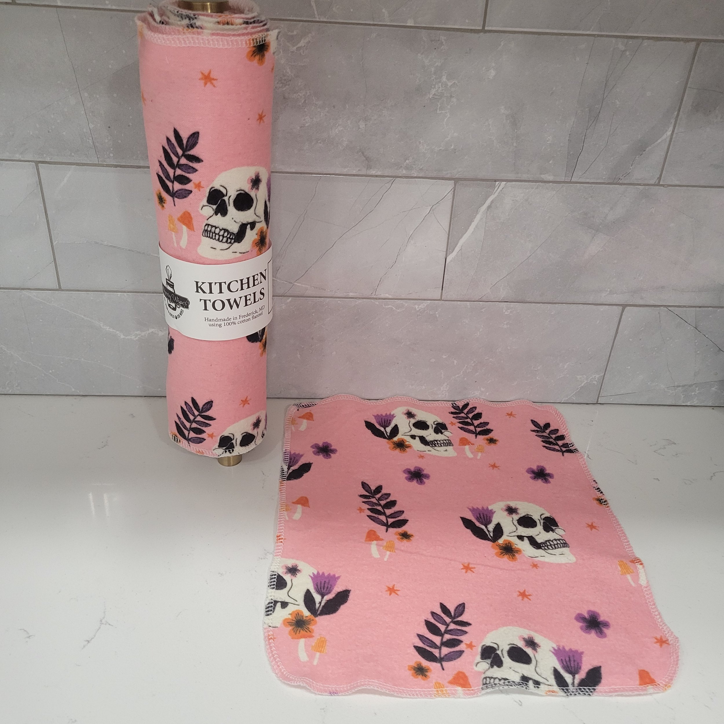 Reusable kitchen towel showing skulls amongst ferns with a bubblegum pink background, plus a single towel