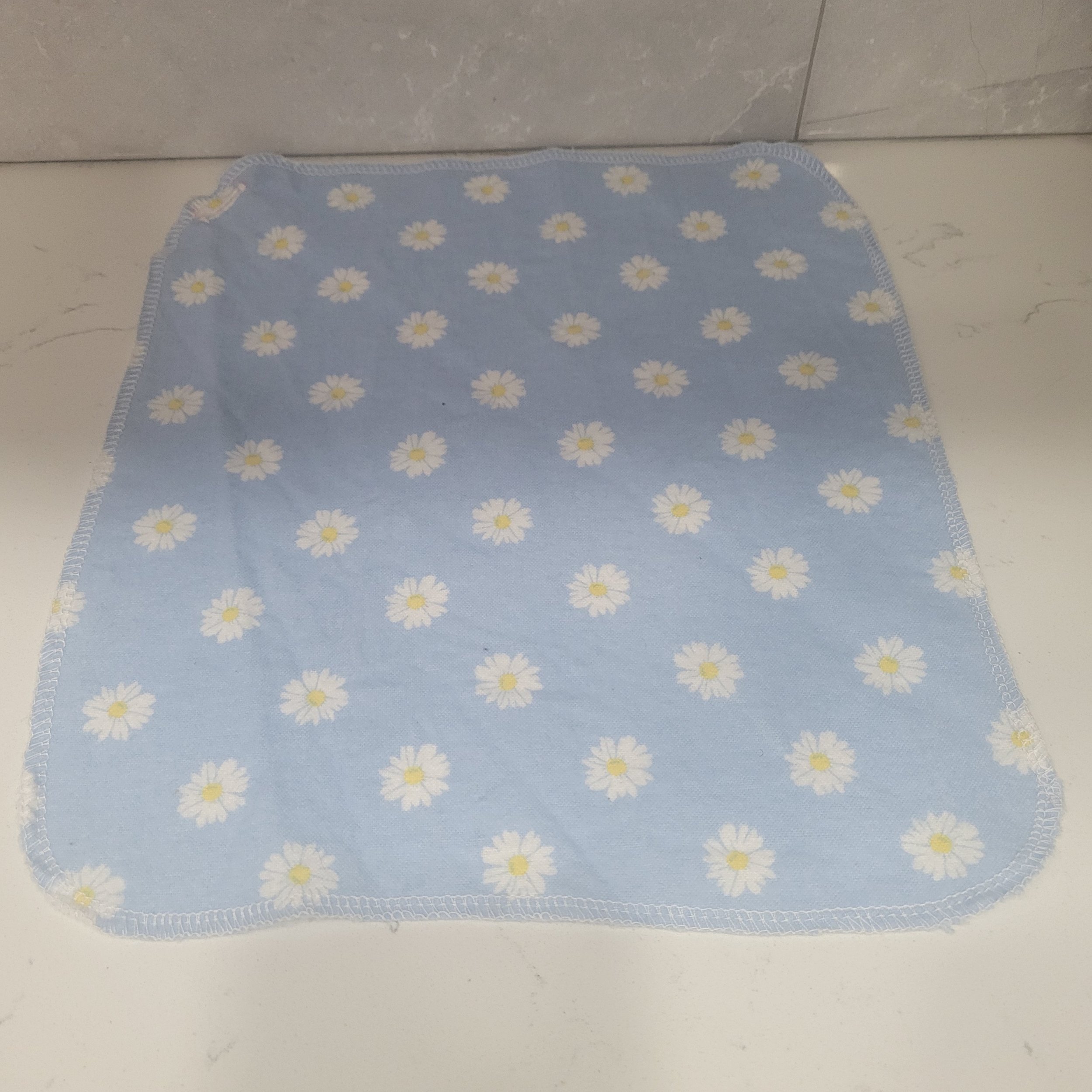 Reusable flannel cloth showing white daisies on a blue background. Each Go Wipe has a sewn buttonhole for attachment to the included carabiner belt clip