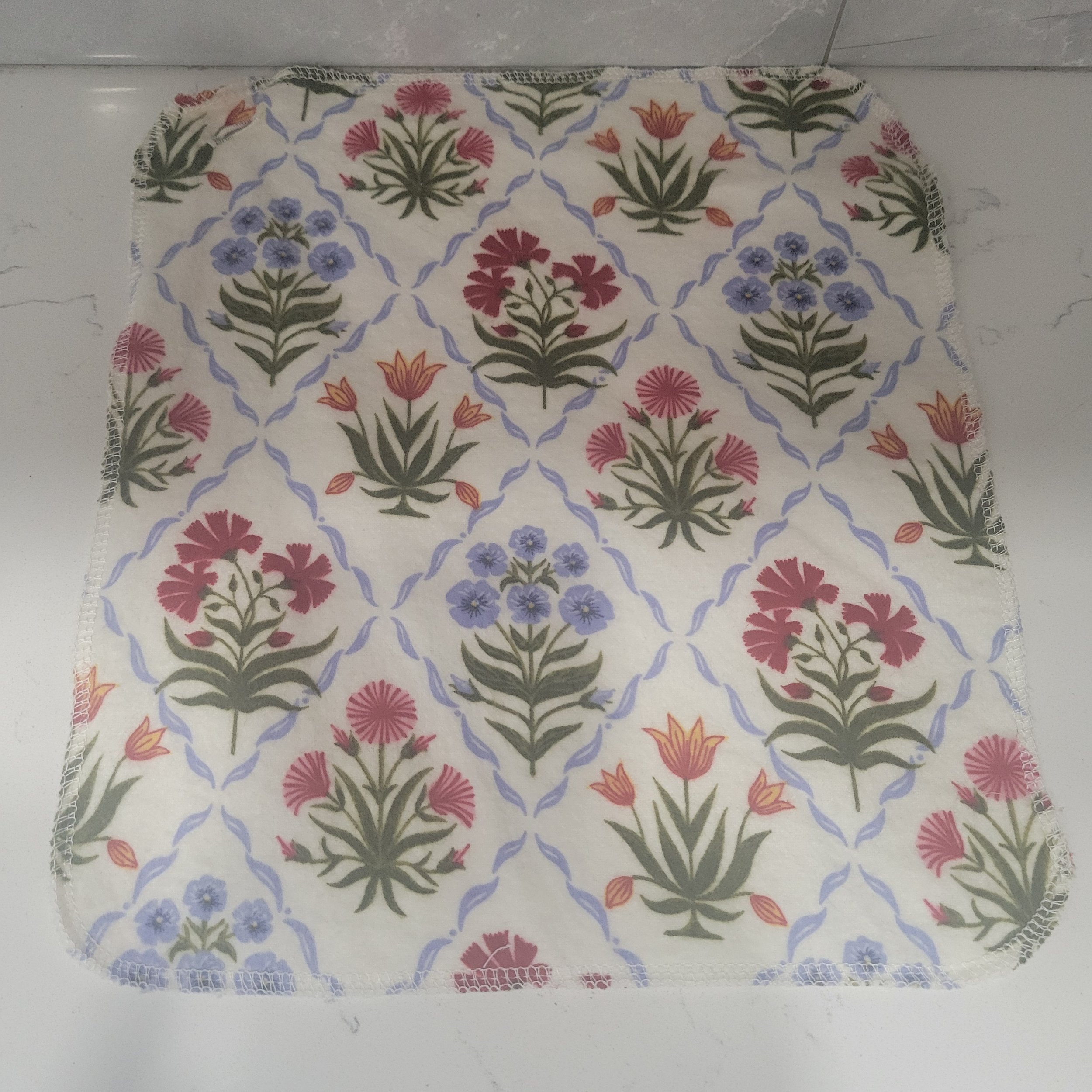 Reusable flannel cloth showing red, yellow and blue wildflowers in diamonds on a white background. Each Go Wipe has a sewn buttonhole for attachment to the included carabiner belt clip