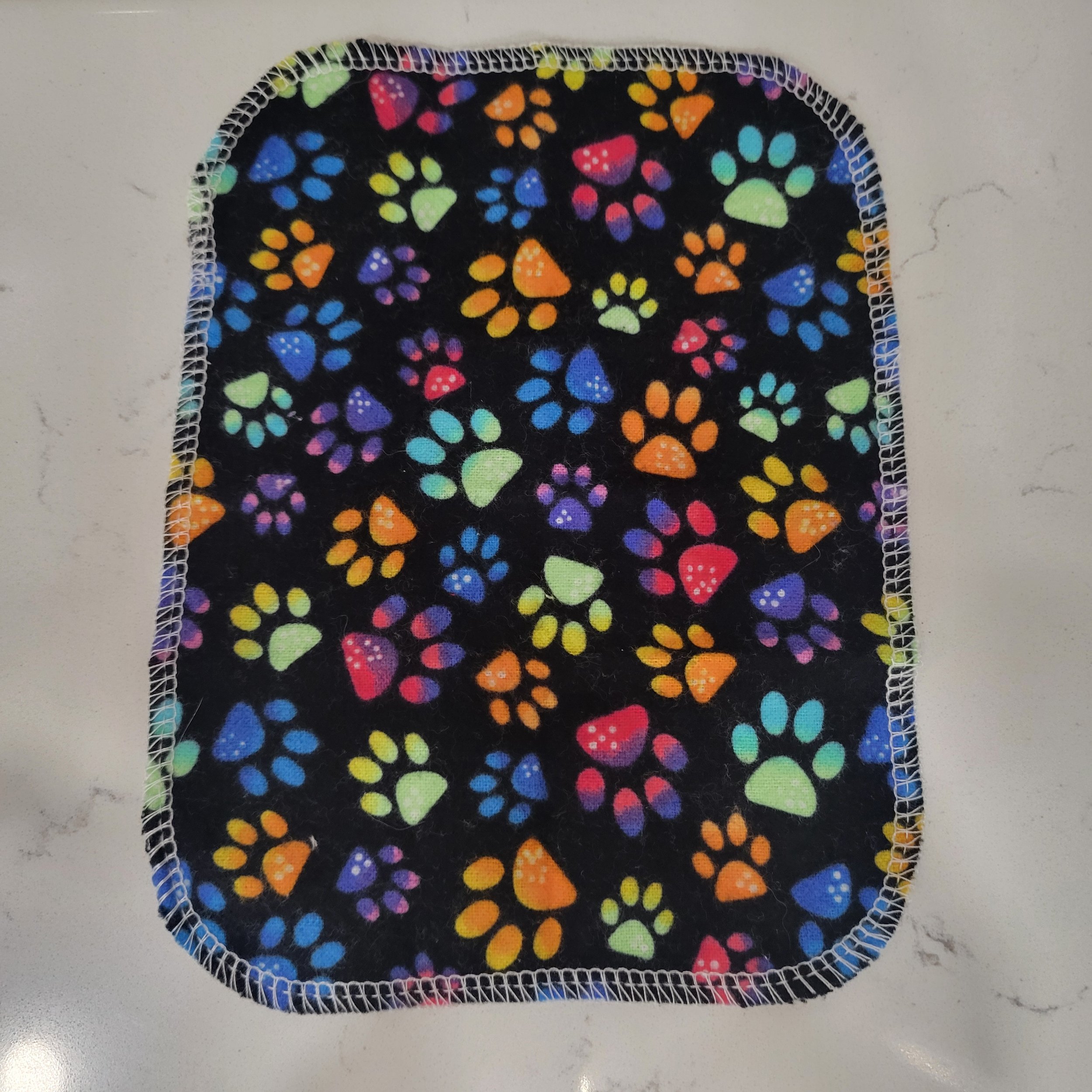Single reusable tissue showing brightly colored paw prints on a black background