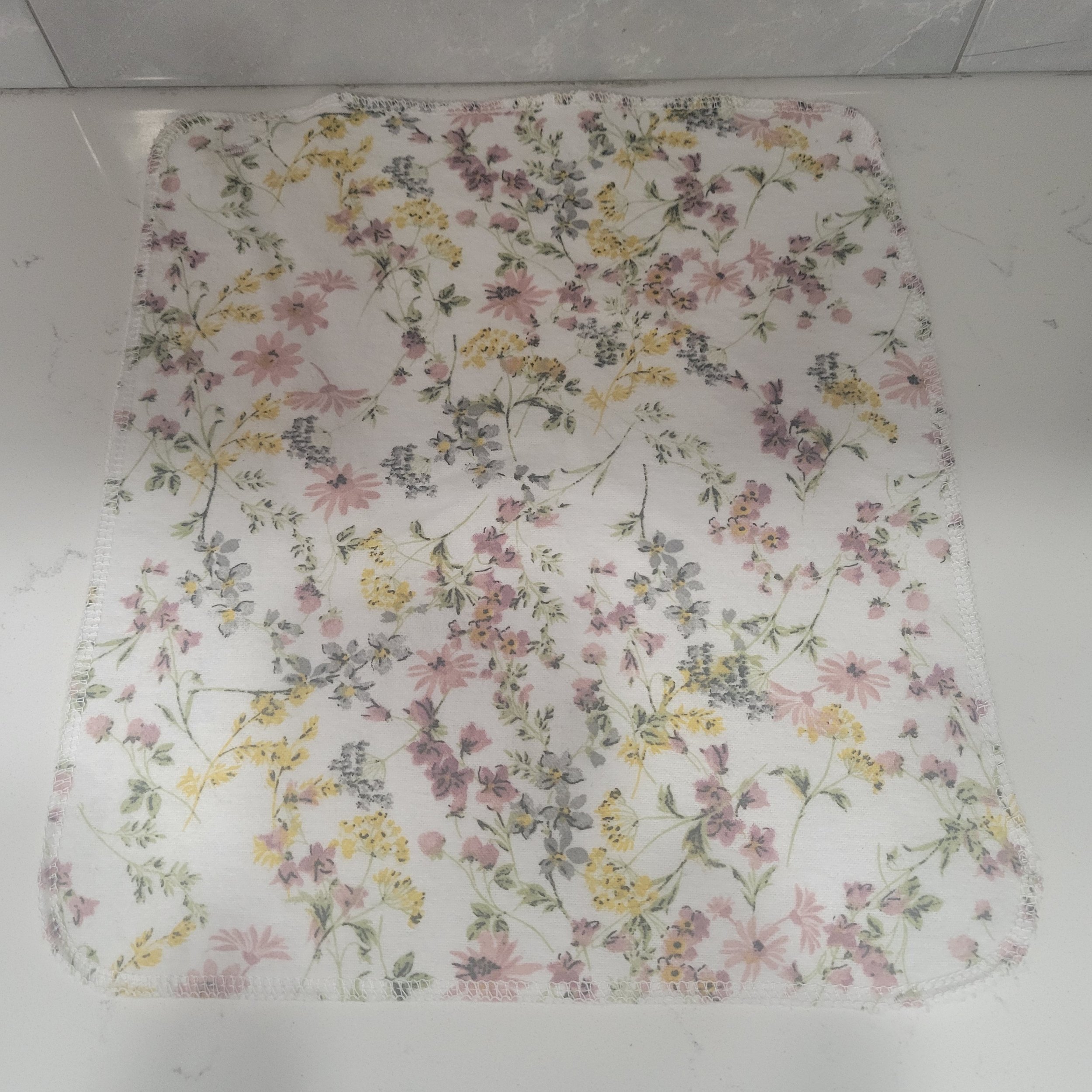 Reusable flannel cloth showing tiny wildflowers on an off-white background. Each Go Wipe has a sewn buttonhole for attachment to the included carabiner belt clip