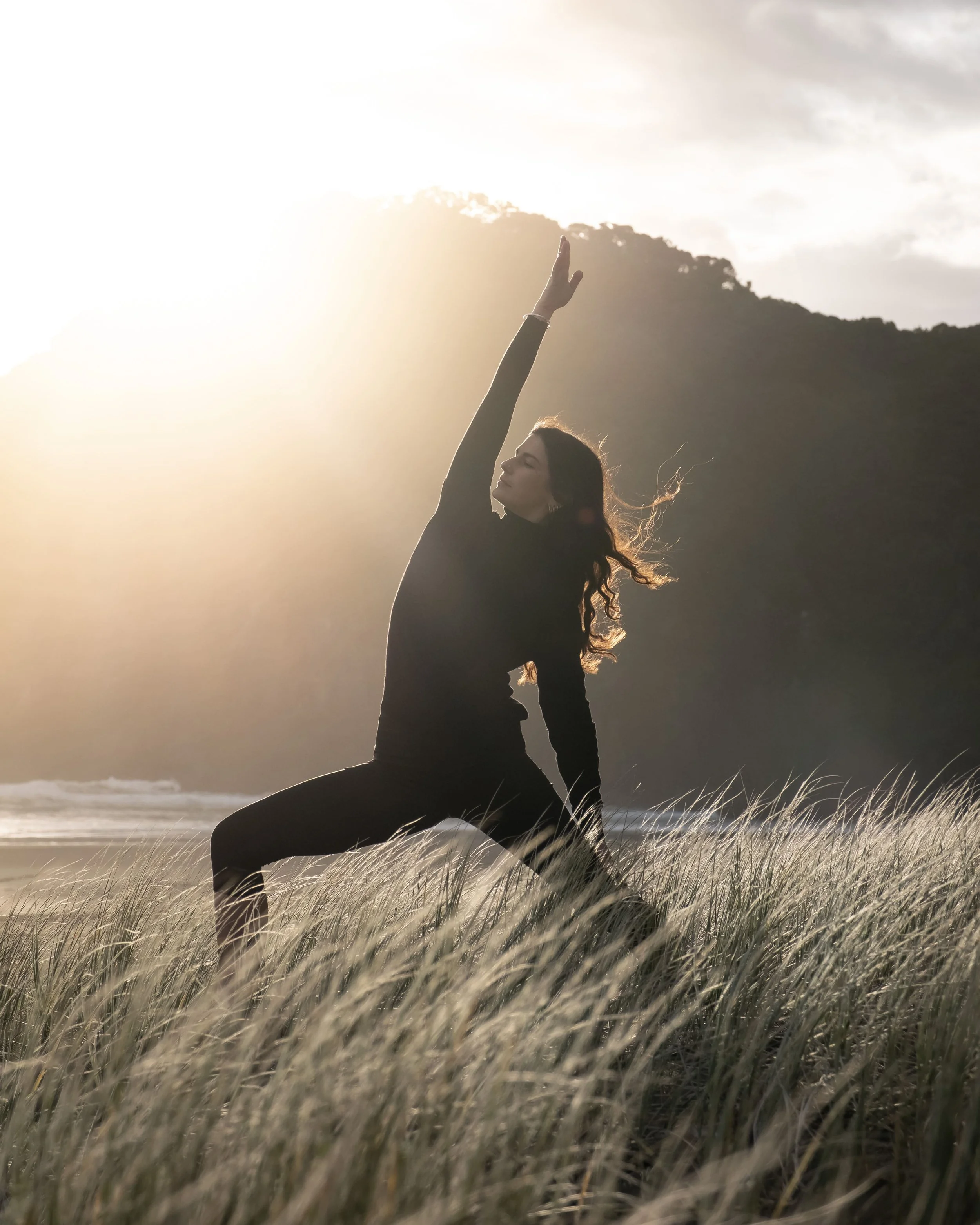 A person practicing yoga in a grassy field at the beach during sunset.