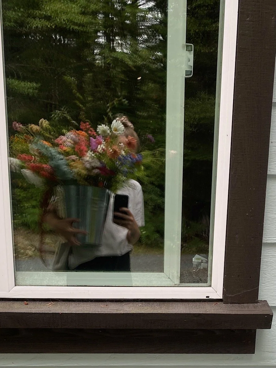 Person taking a photo of a bouquet of flowers reflected in a window.