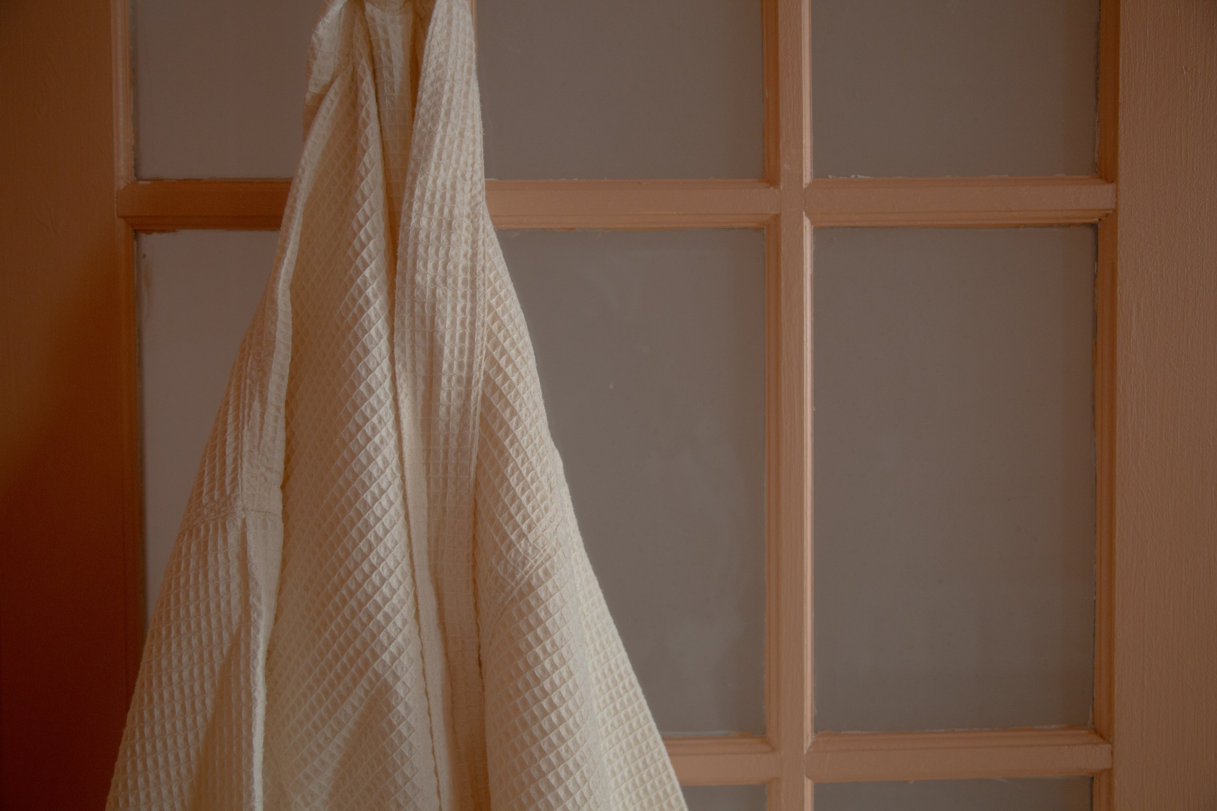 A cream-colored textured towel hanging on a wooden door with glass panes.