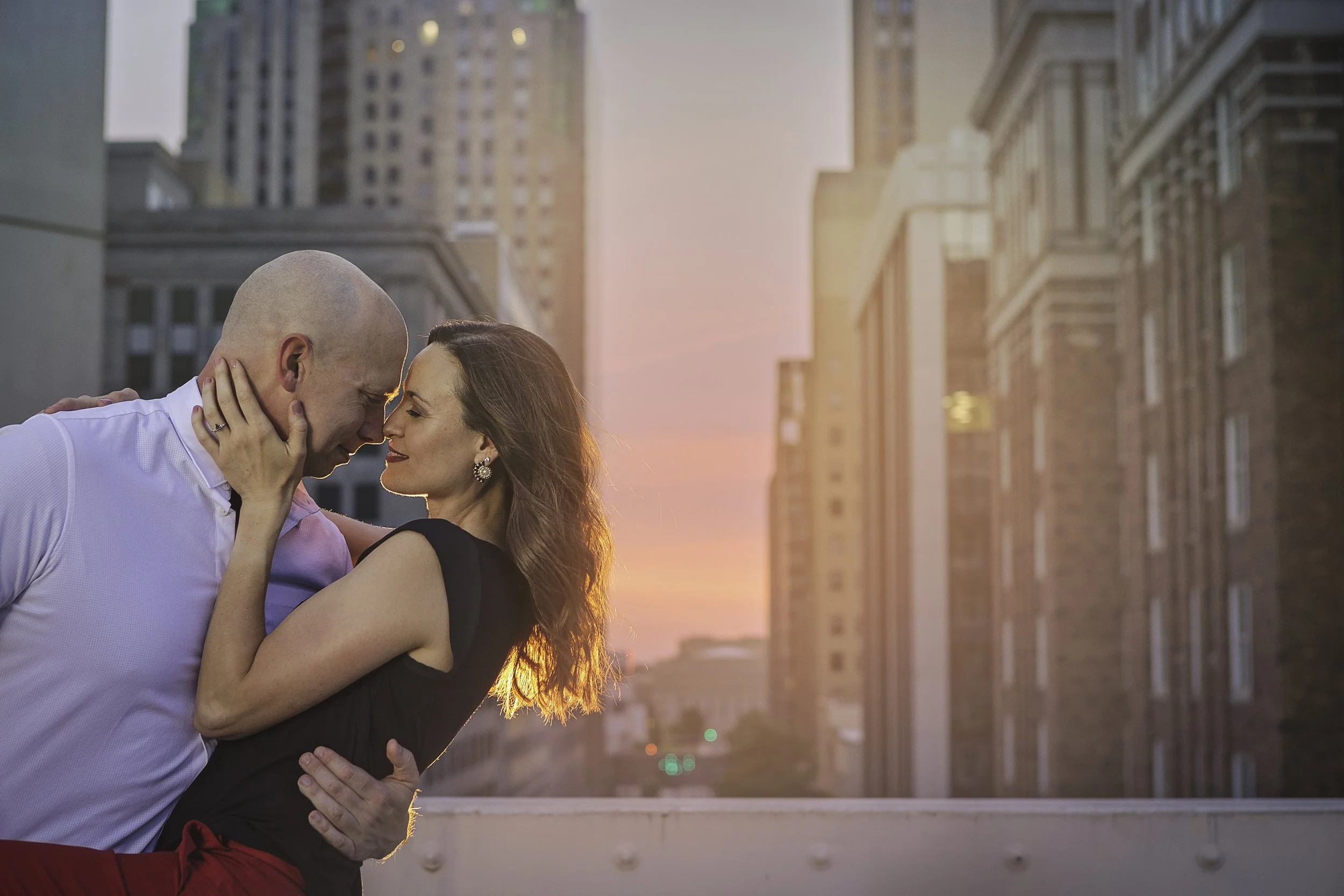 Rooftop engagement session with city buildings in the background at sunset.