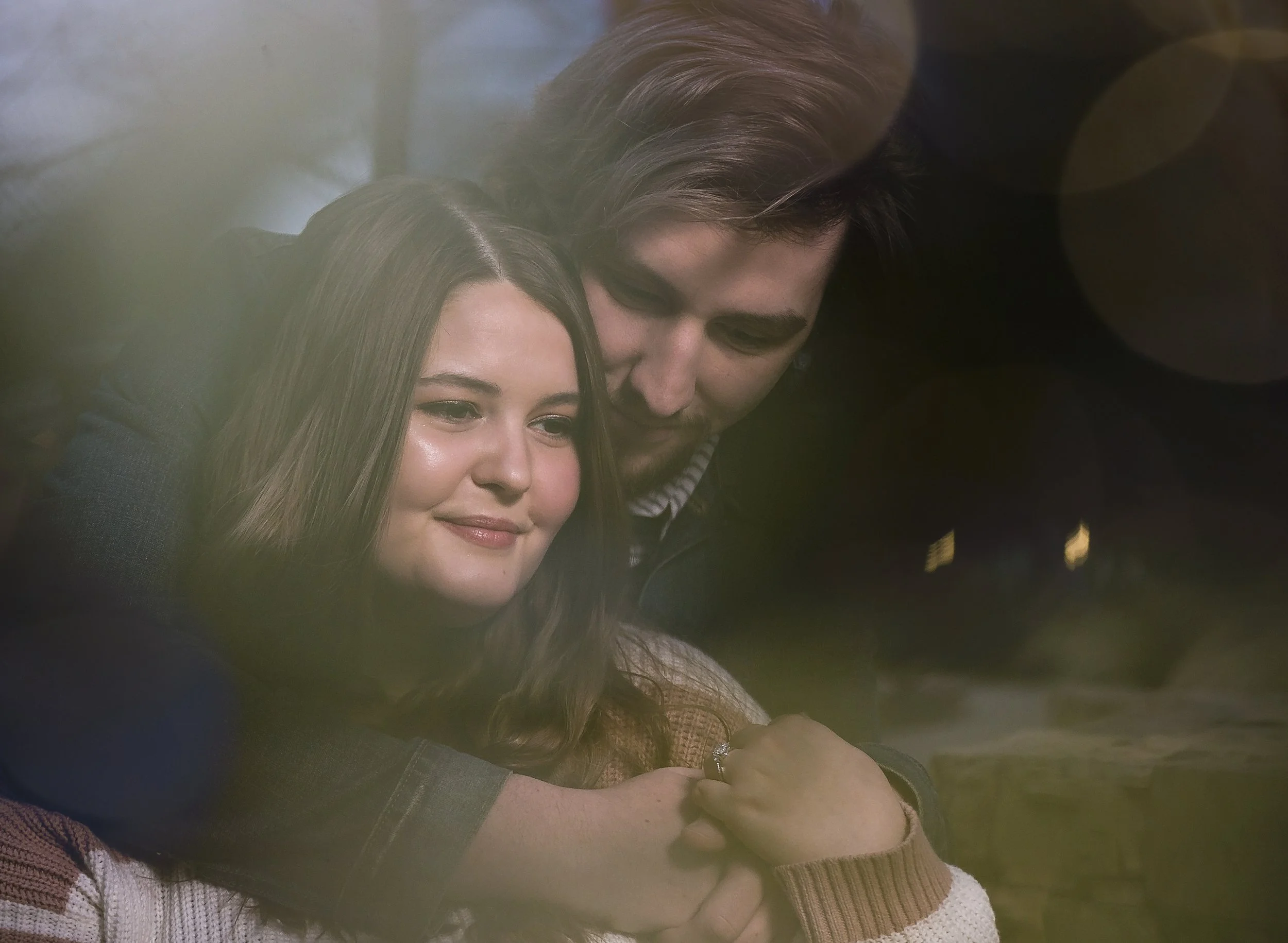 A young couple sharing a hug, with the woman smiling and the man leaning in close, both appearing to be happy.