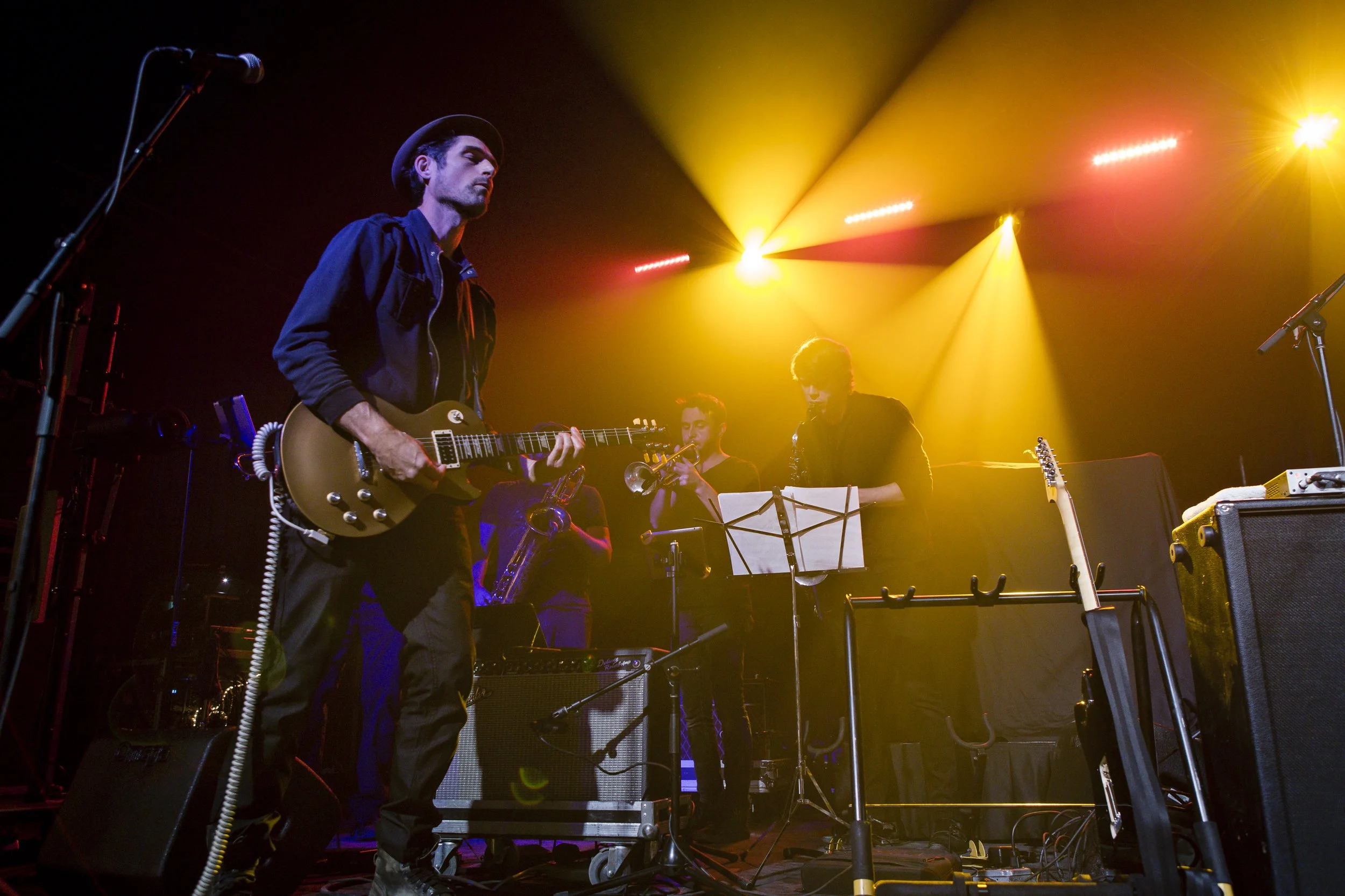 Musicians playing instruments on stage under colorful lights during a live performance.