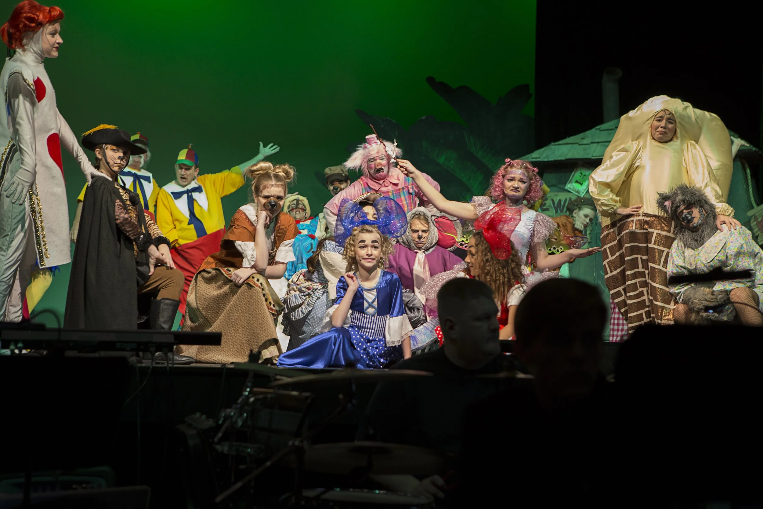 Children in colorful costumes performing on stage as characters from The Wizard of Oz including the Tin Man, Scarecrow, and Dorothy.