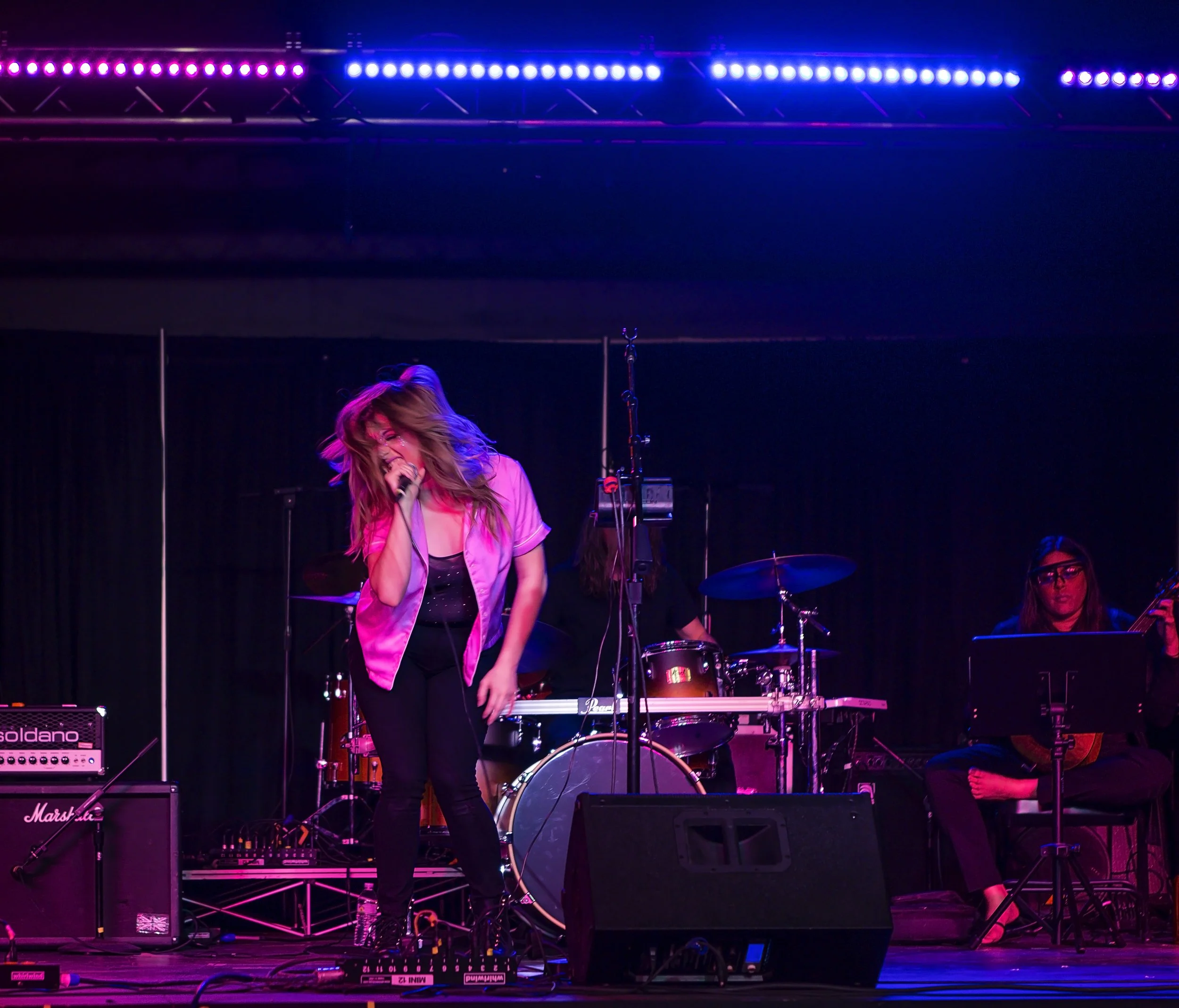 Female singer performing on stage with band, purple lighting