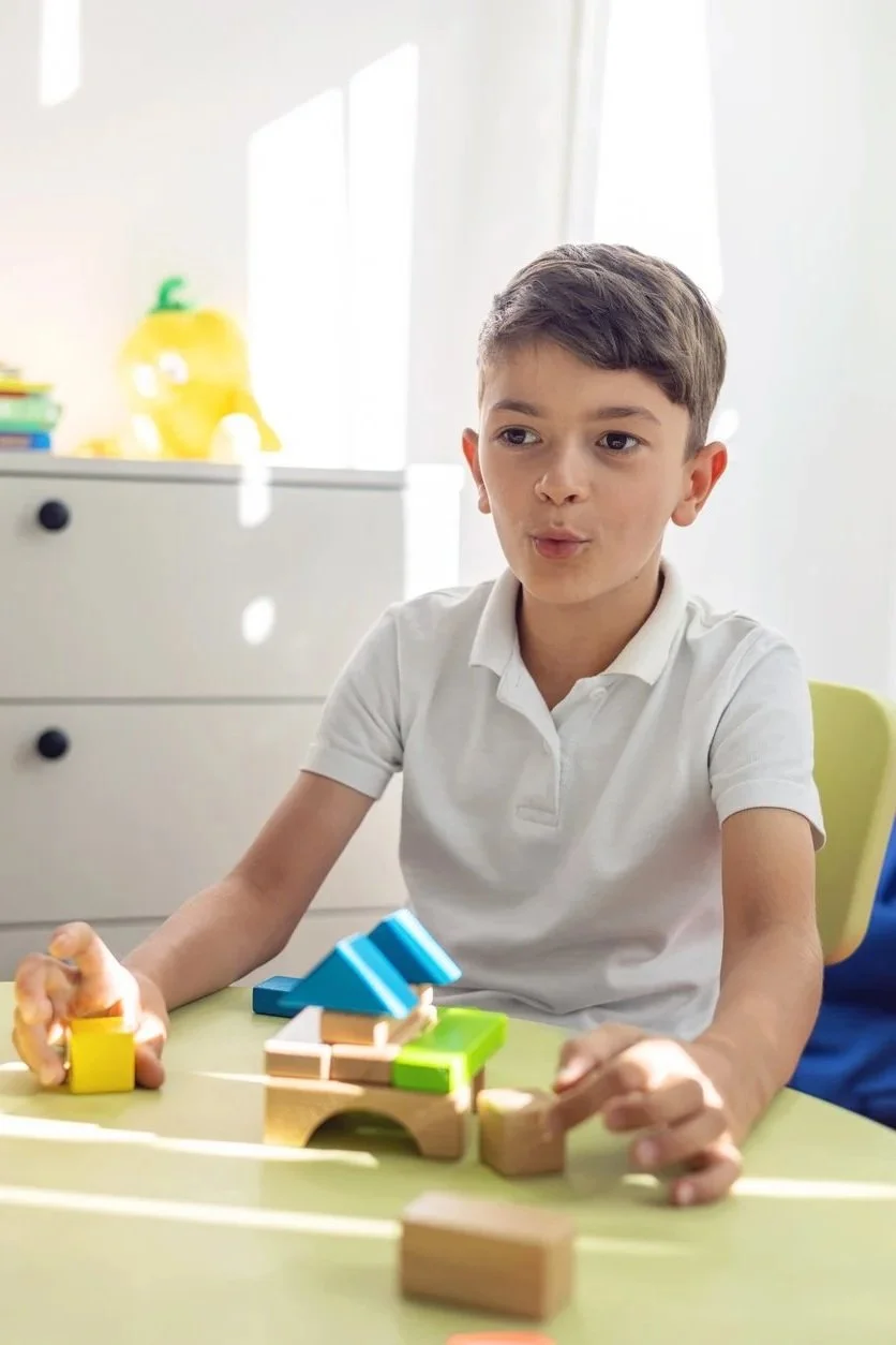 A boy playing with wooden and plastic building blocks at a table.
