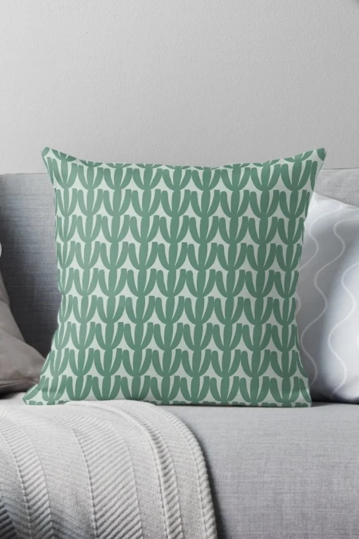 Decorative pillow with green cactus pattern on a gray sofa with a white blanket.
