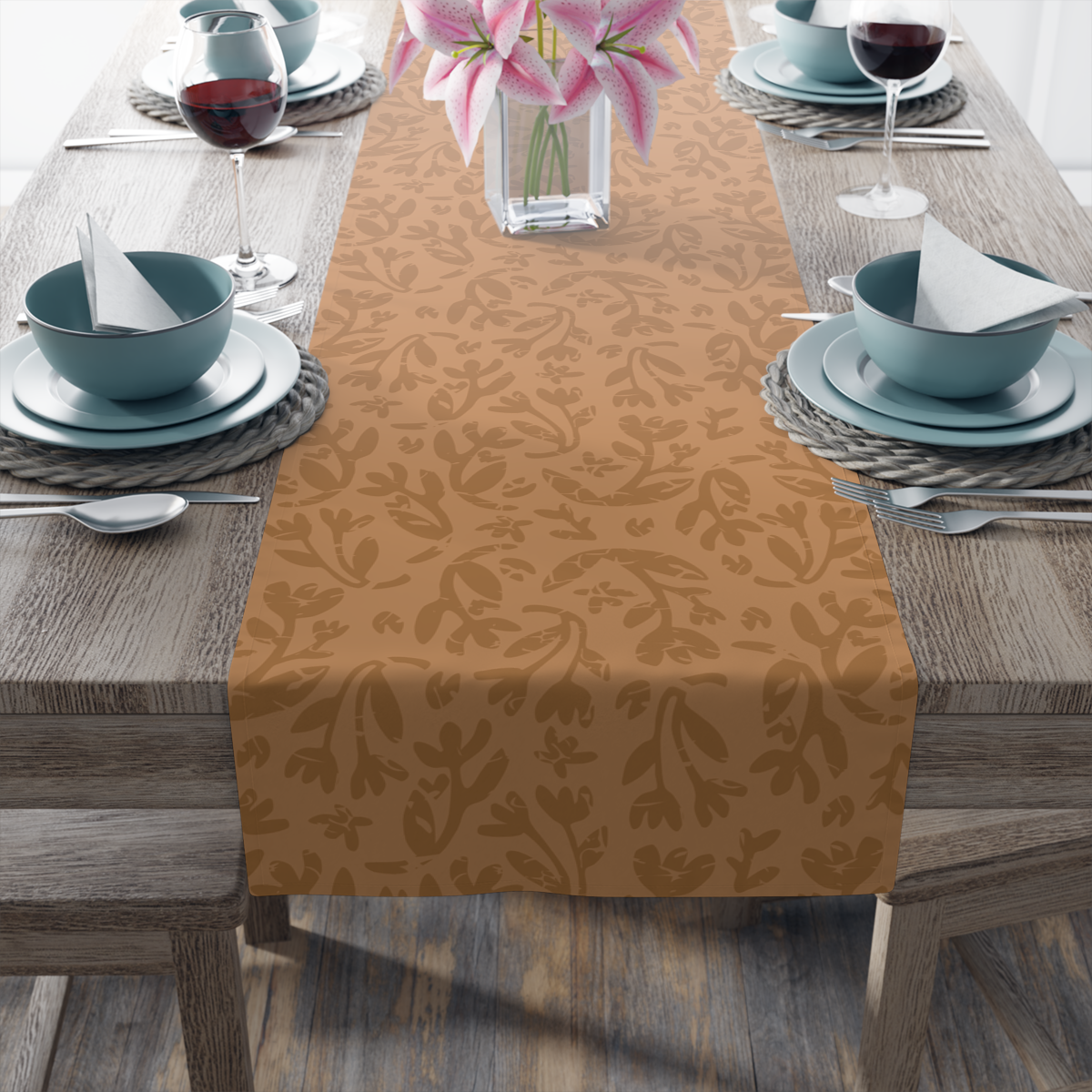 Dining table set with teal bowls, wine glasses, and a floral-patterned table runner, featuring a vase with pink lilies.