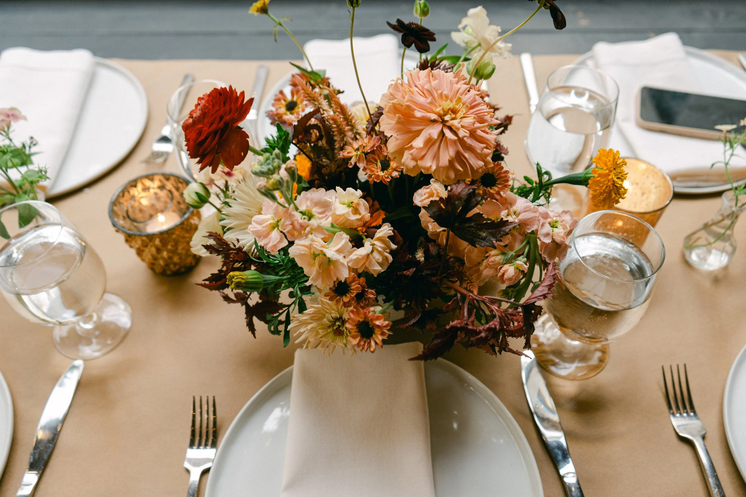 wedding flower centerpiece with ranunculus, zinnias, and chocolate cosmos. Flowers are in a bright fall palette and arranged with a garden design style. 
