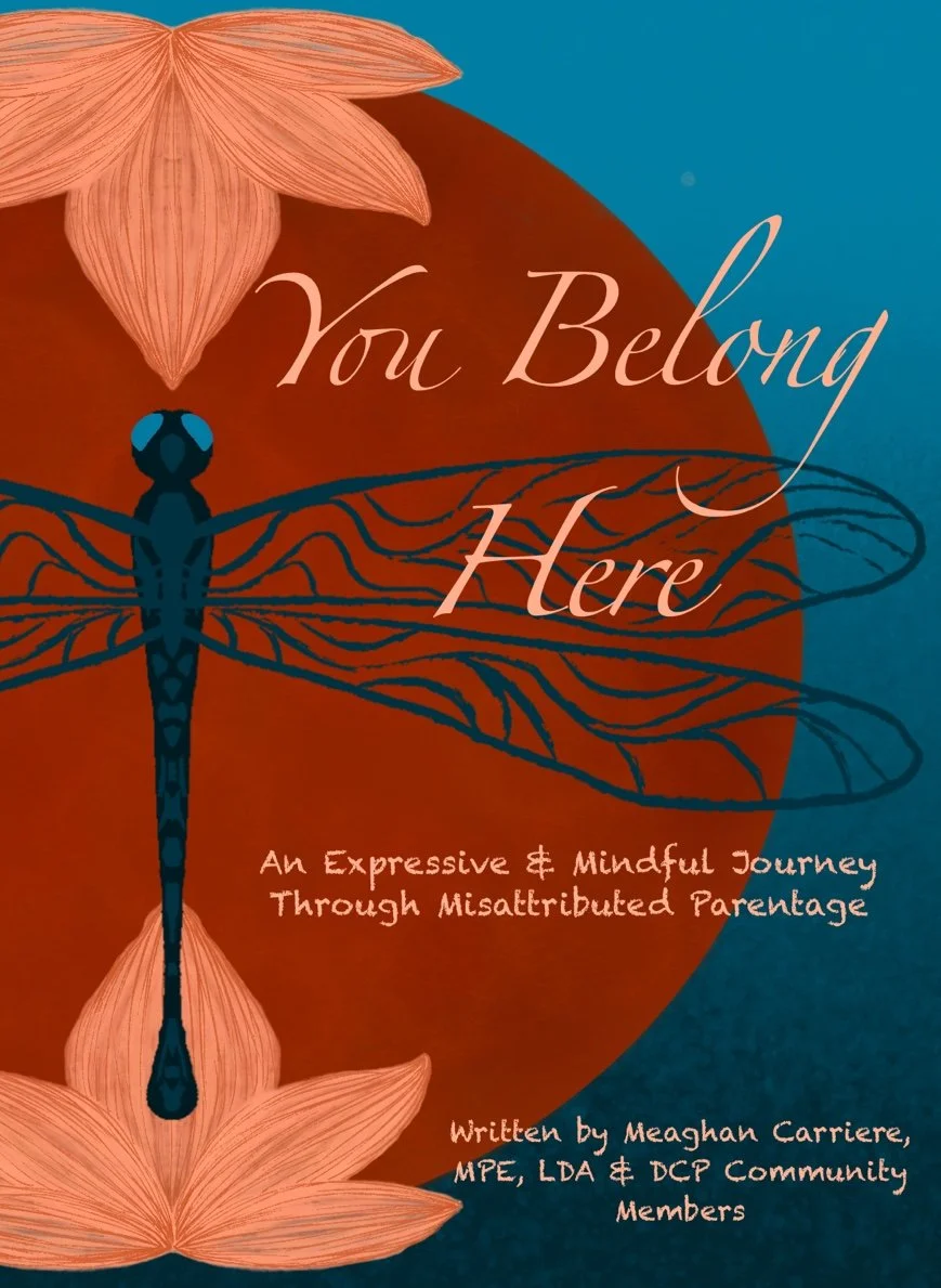 Book cover titled 'You Belong Here' with an illustration of a dragonfly, flowers, and a background with blue and orange tones. Subtitle reads 'An Expressive & Mindful Journey Through Misattributed Parentalage.' Written by Meaghan Carriere, MPE, LDA & DCP Community Members.
