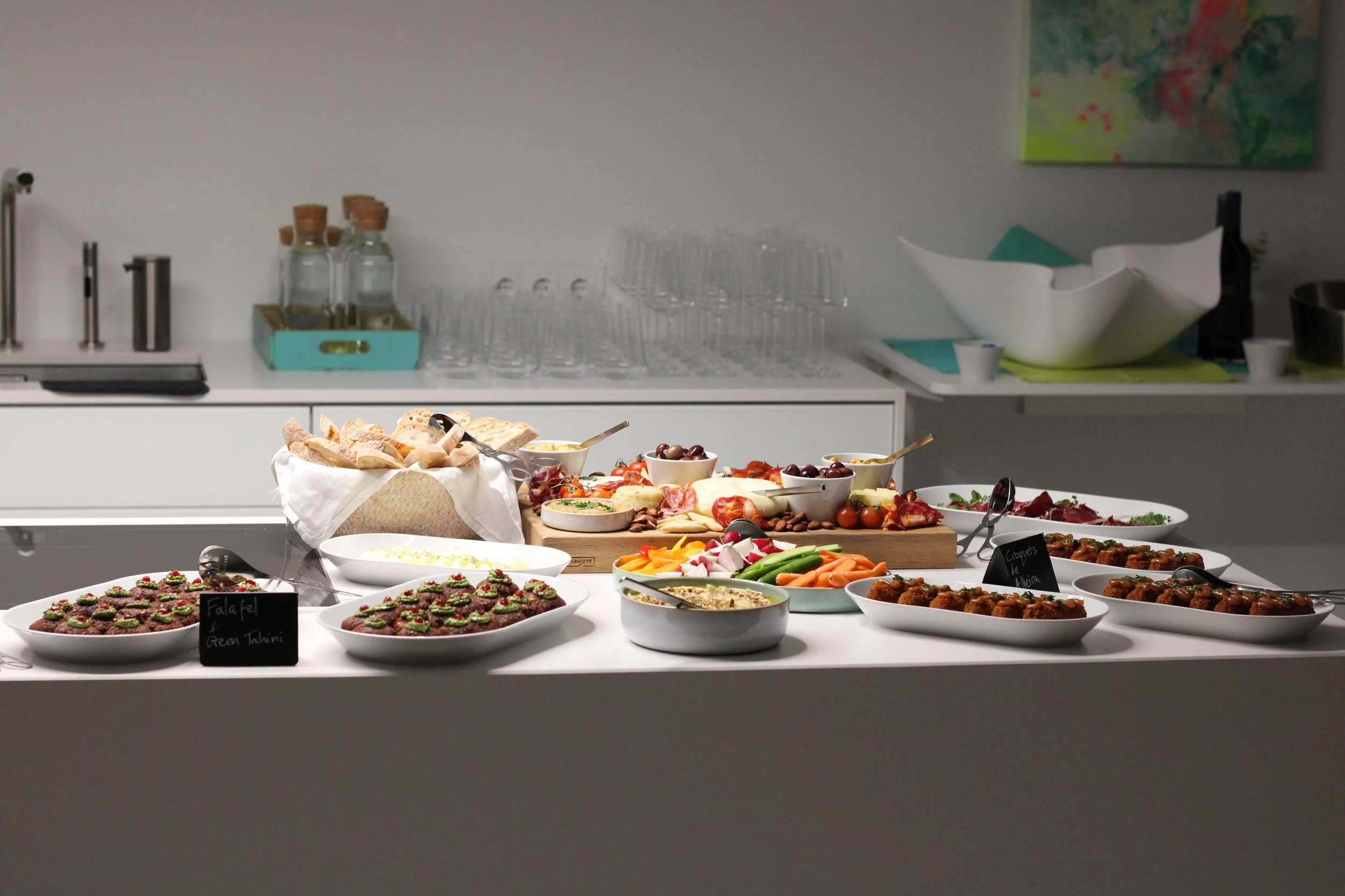 Cheese and bread platter with various cheeses, sliced breads, olives, and garnishes on a table.