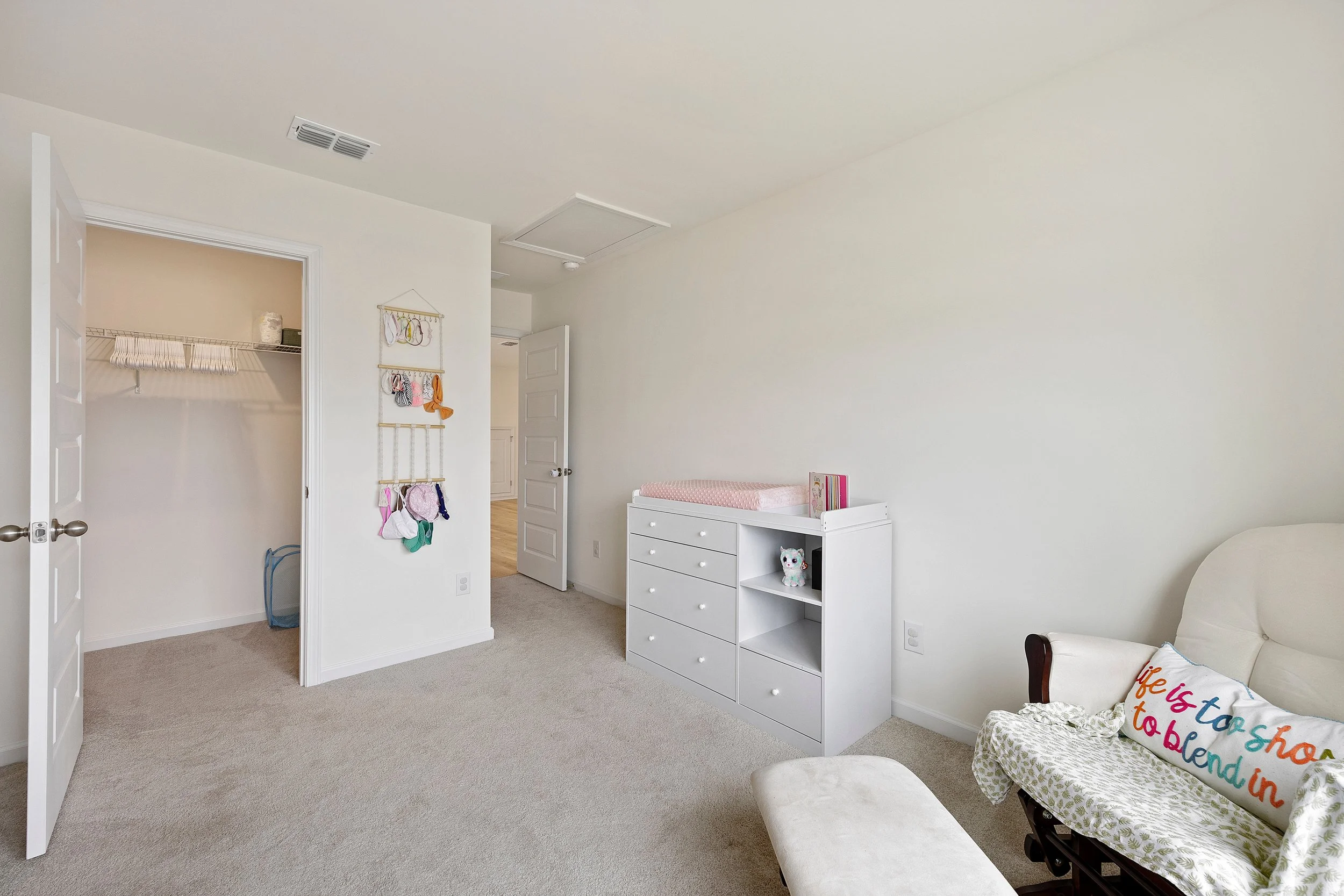 A bedroom with a closet, dresser, and a white armchair with a colorful pillow that says 'Life is too short to blend in'.