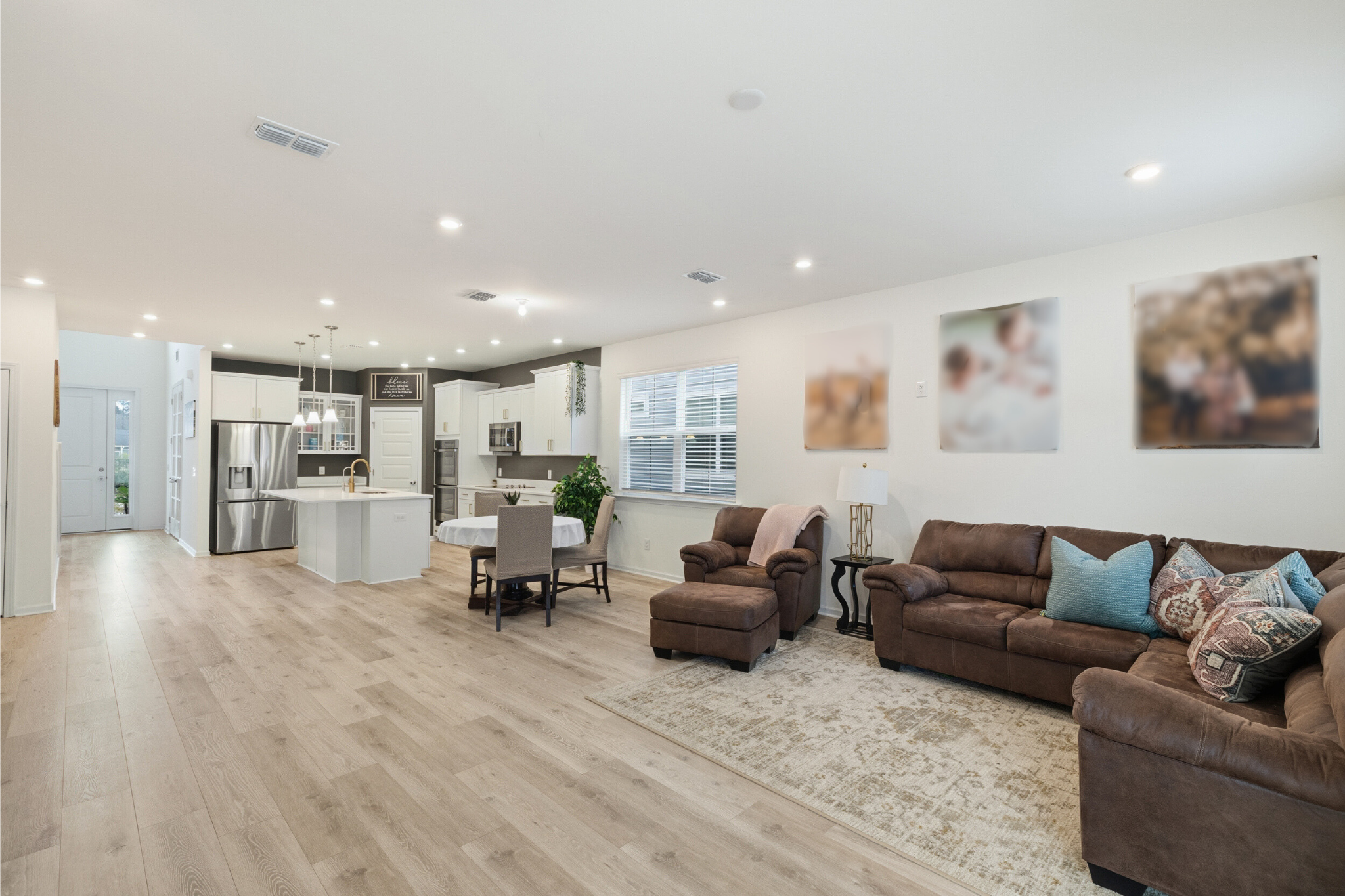 Open-concept living room and kitchen area in a modern home with white walls, wooden floors, and contemporary furniture.
