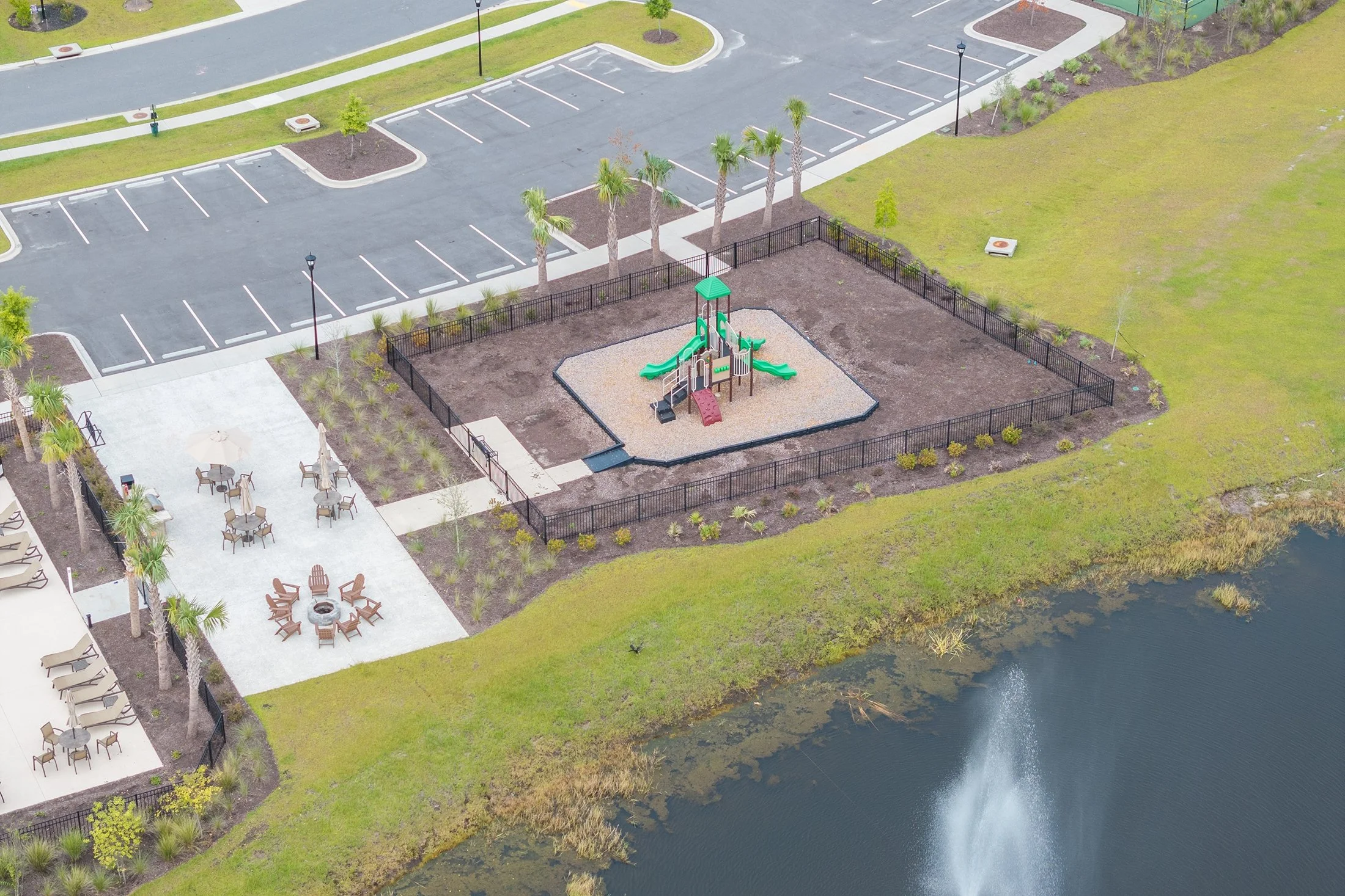 An aerial view of a park with a playground, parking lot, picnic area, and a pond.