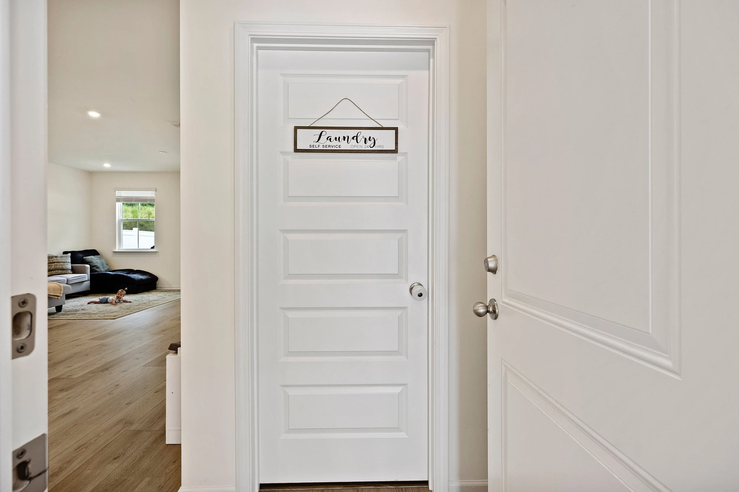 View of a white interior door with a laundry sign hanging on it, leading into a living room with a dog lying on a rug.