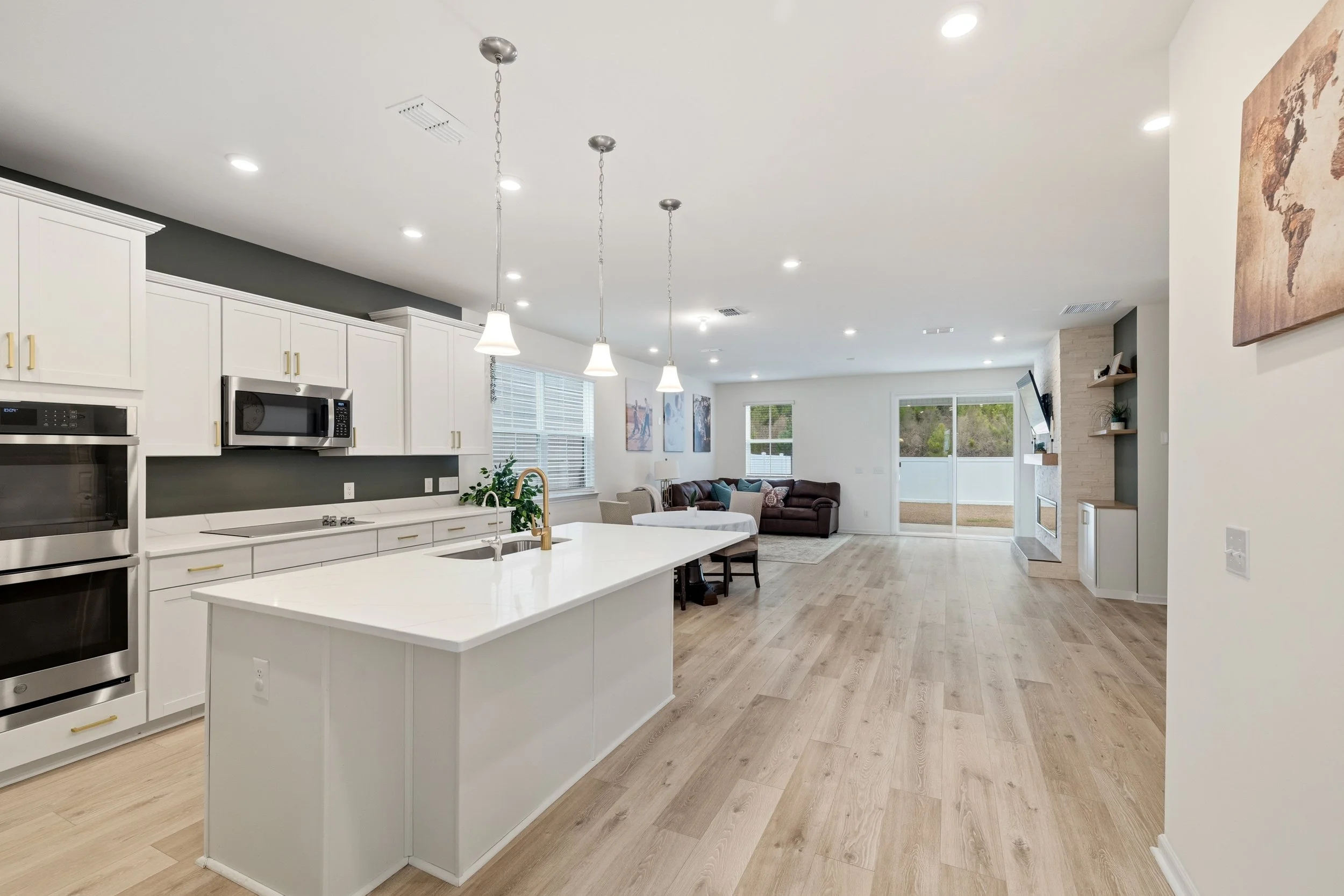 Open-concept kitchen and living room with white cabinets, a large island with a sink, hardwood floors, and a seating area with a sofa and a dining table.