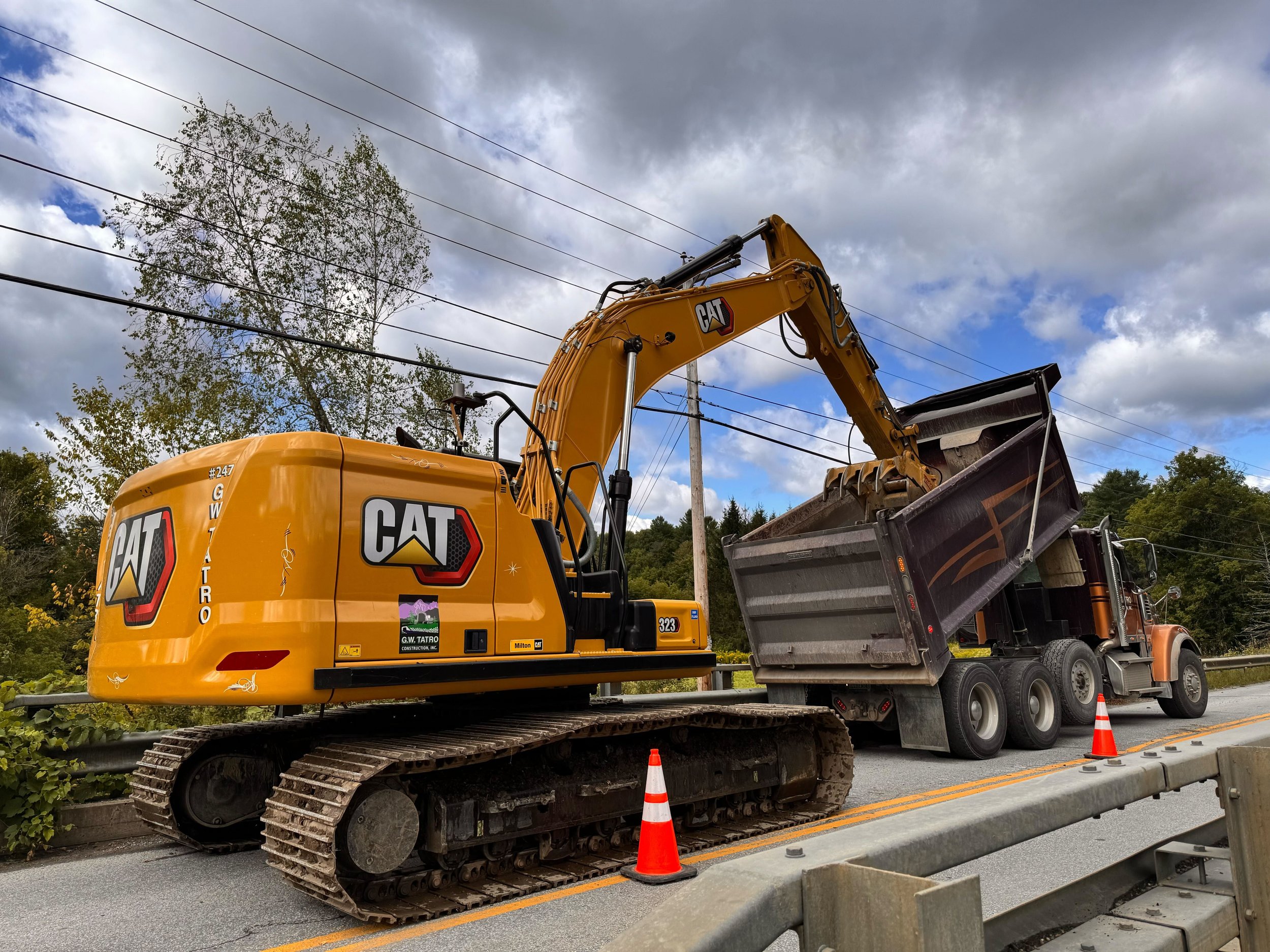 Two yellow excavators digging and moving rocks near a water body at a construction site with a cloudy sky.