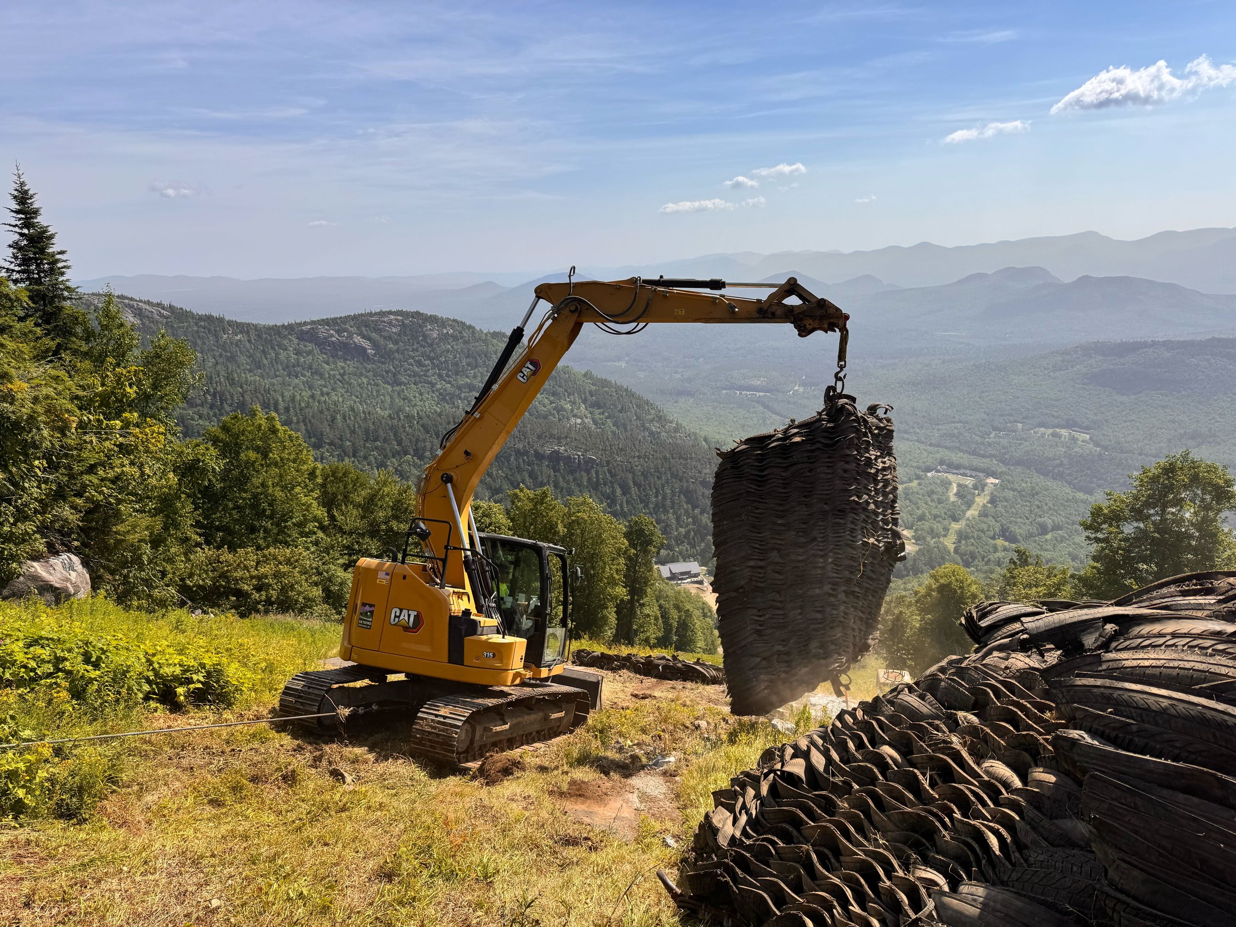 A yellow Caterpillar excavator working on a snowy mountain terrain.