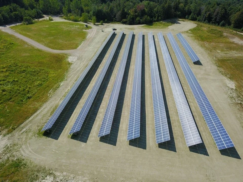 Aerial view of multiple solar panels installed in a large open area surrounded by trees and greenery.