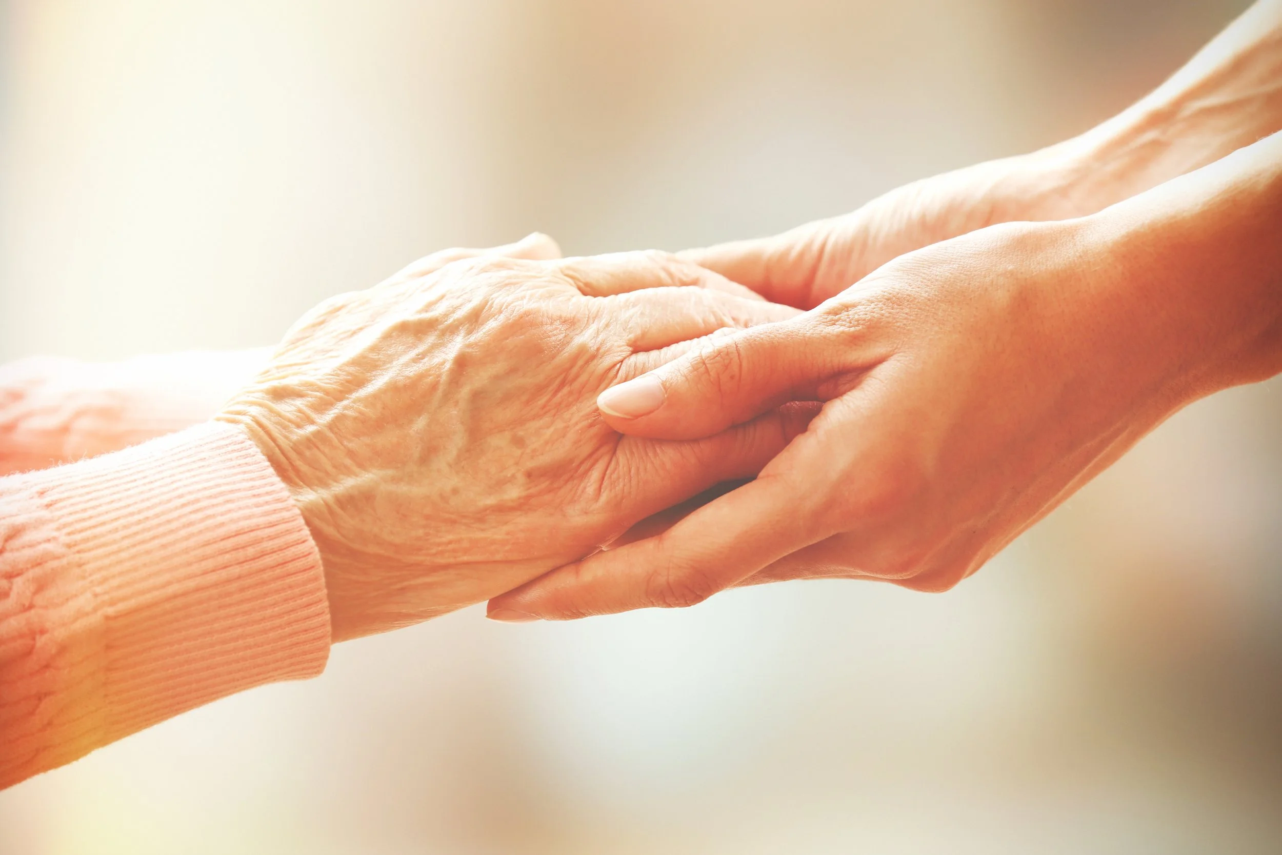 A younger person holding the hand of an elderly person.