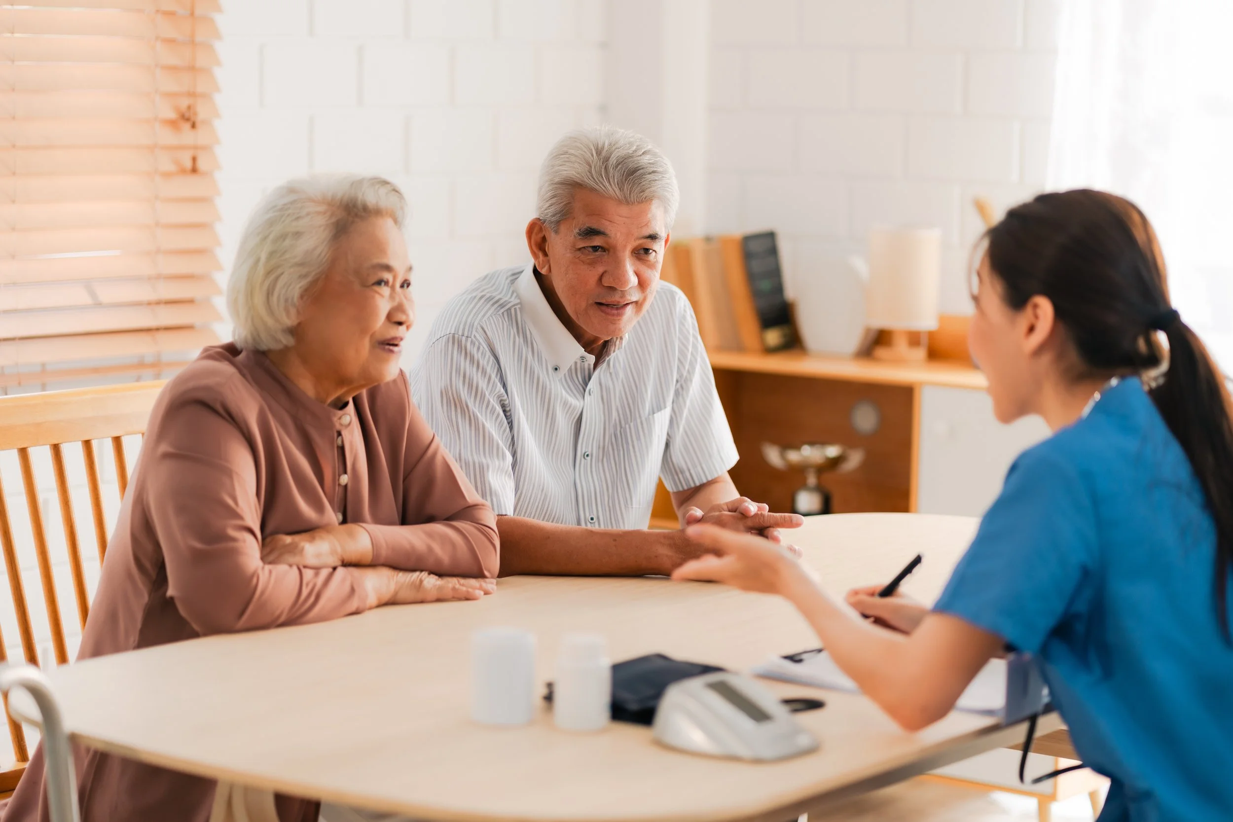 An elderly couple sitting at a table with a healthcare professional in a blue uniform, engaging in a discussion.