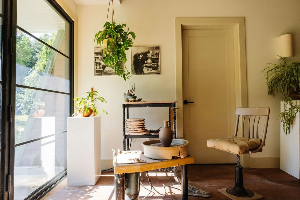 Interior of a room with a sliding glass door, plants, artwork, and a wooden chair.