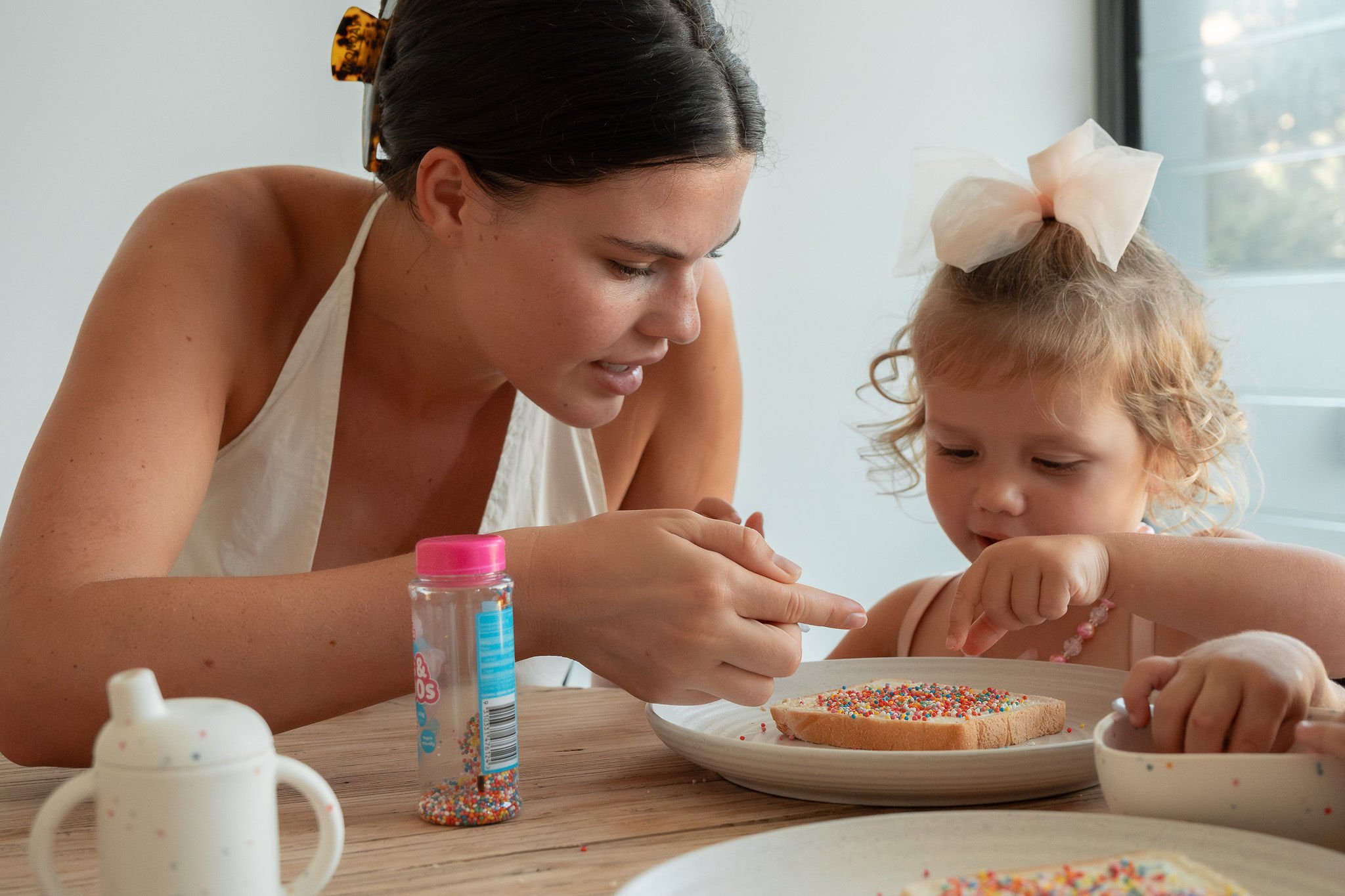 A woman and a young girl decorating a cookie with colorful sprinkles at a table.