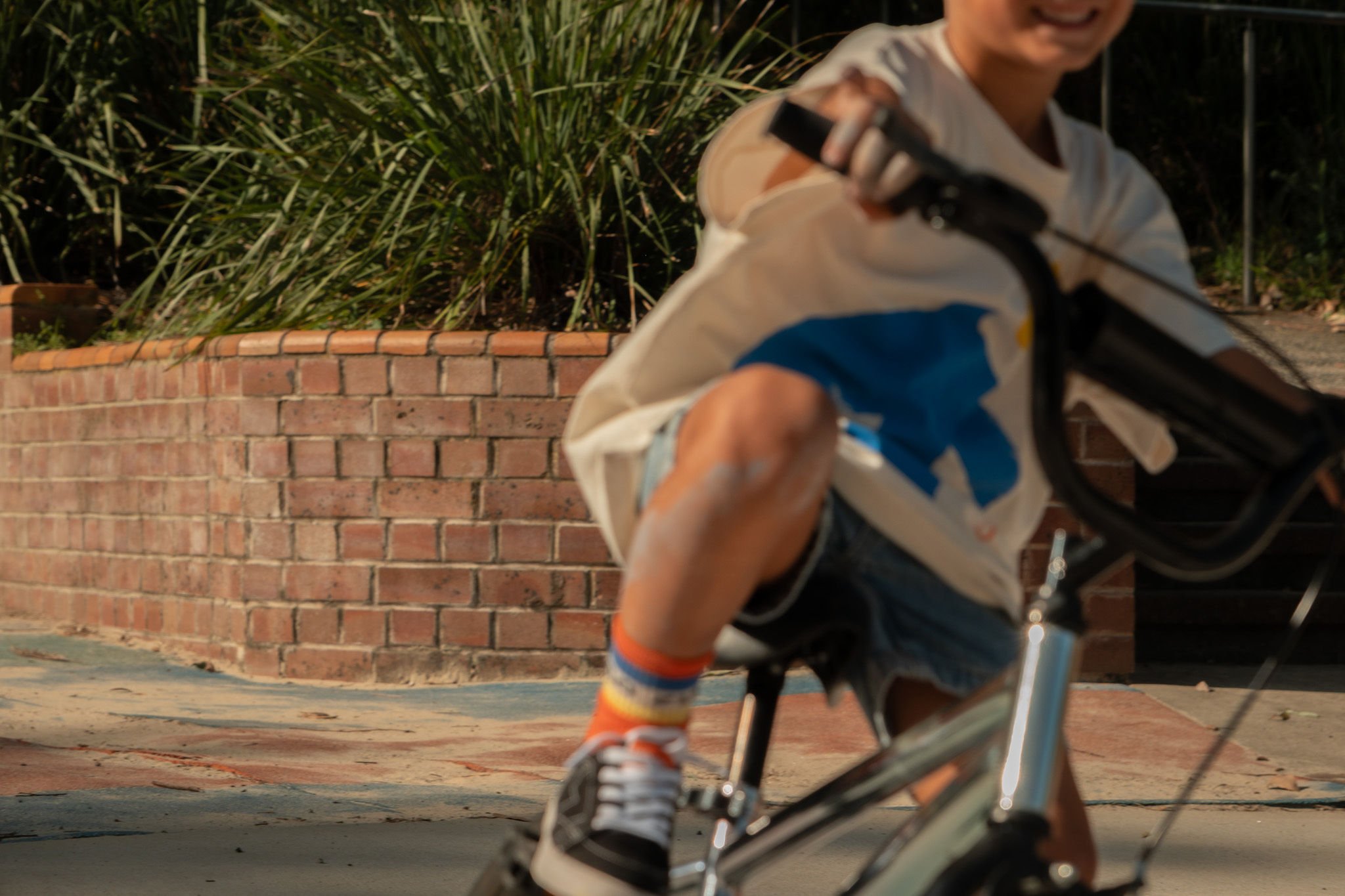 Child riding a bike near a brick wall with greenery in the background."