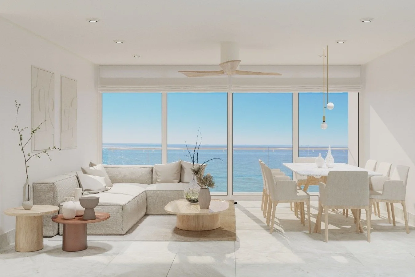 Sala de estar con vista al mar, sofá beige, mesas de madera, plantas decorativas, comedor con sillas blancas y pantalla grande con ventanas panorámicas del océano.