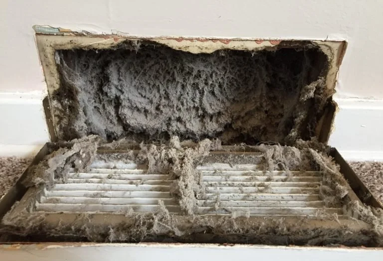 A dirty air vent with dust and debris inside, exposed after the cover was removed.