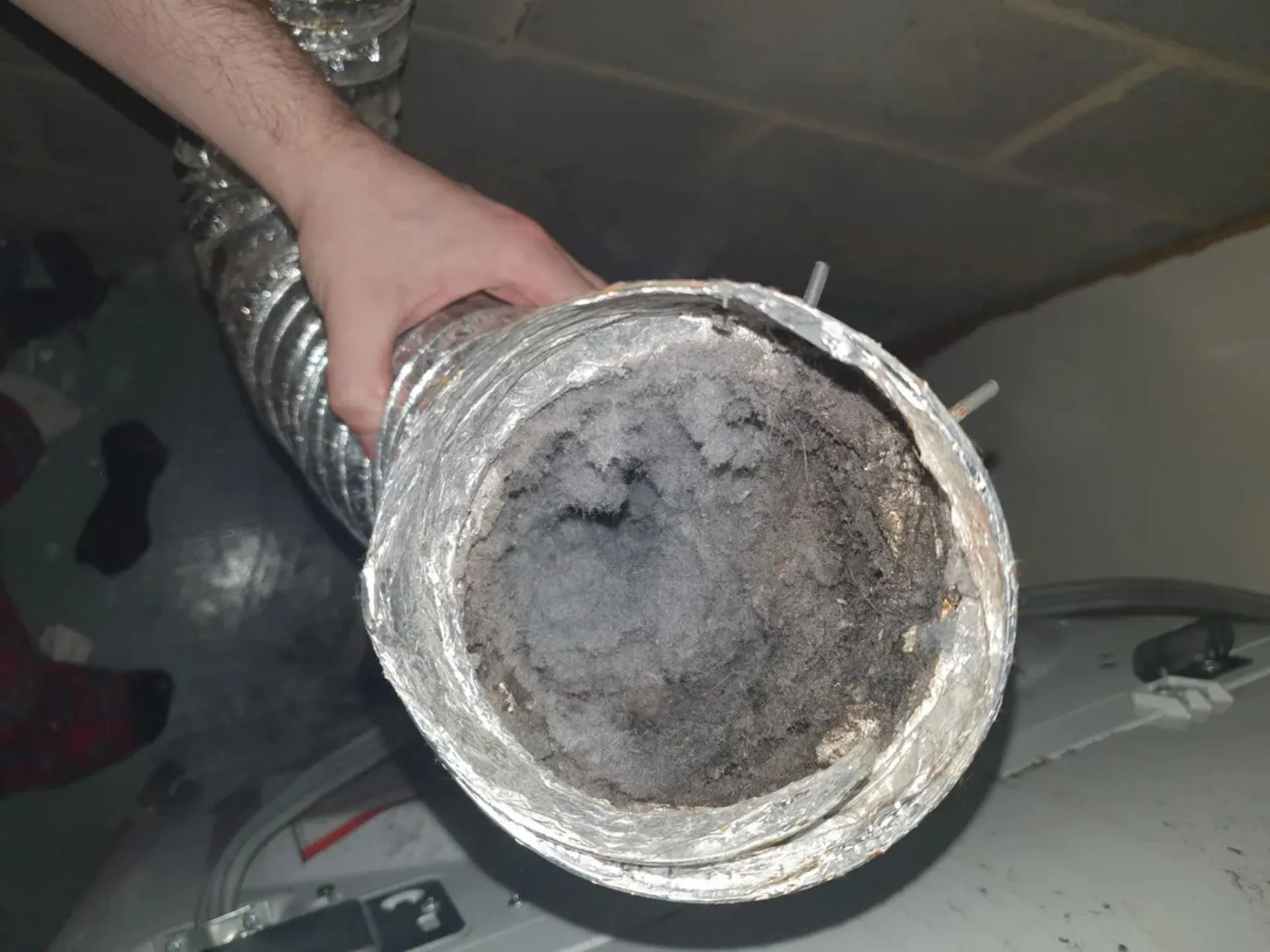 Person holding a dirty metallic pipe or duct with black soot inside.