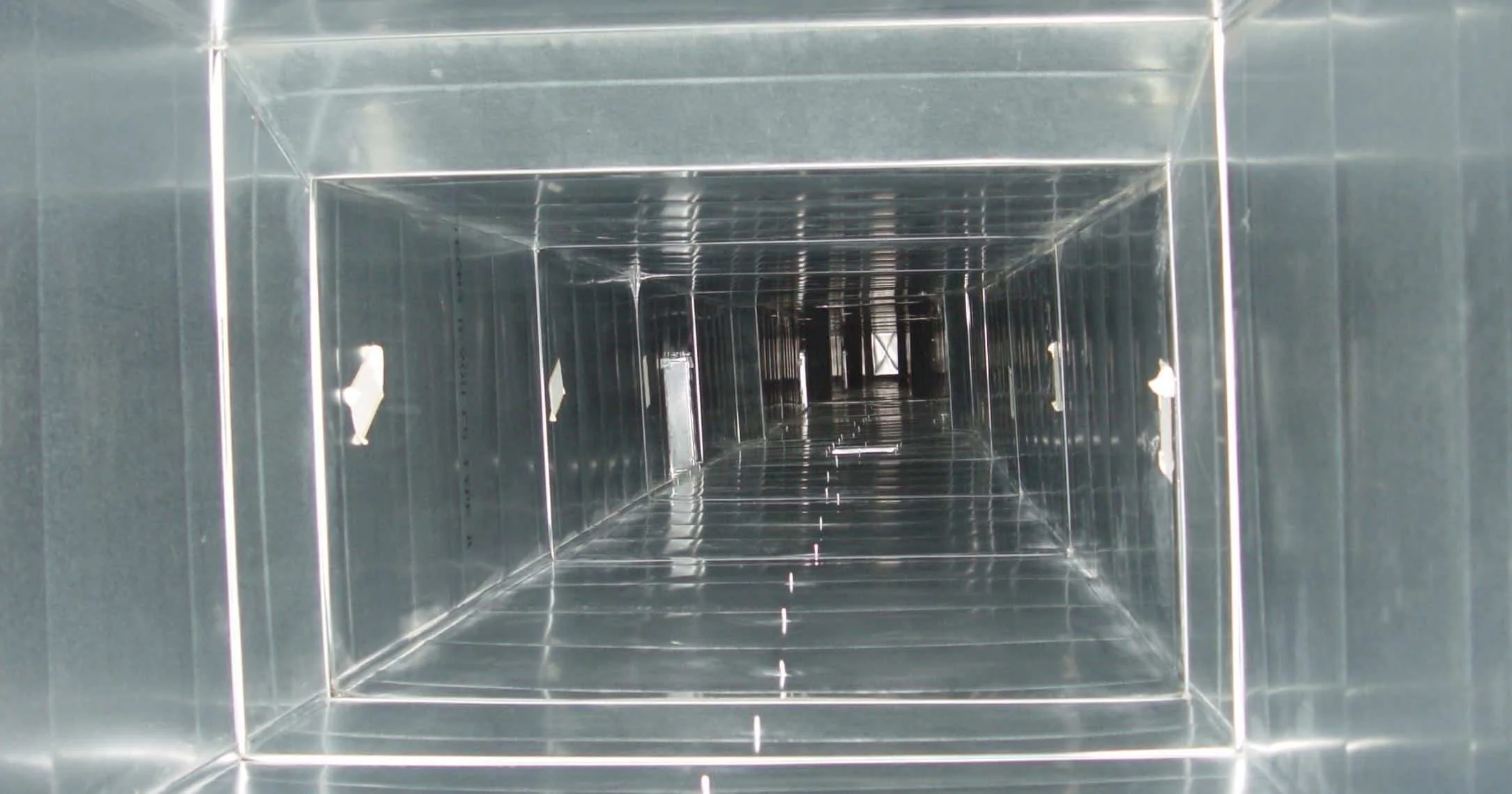 Inside view of a metallic rectangular ventilation duct with reflective surfaces and internal supports.