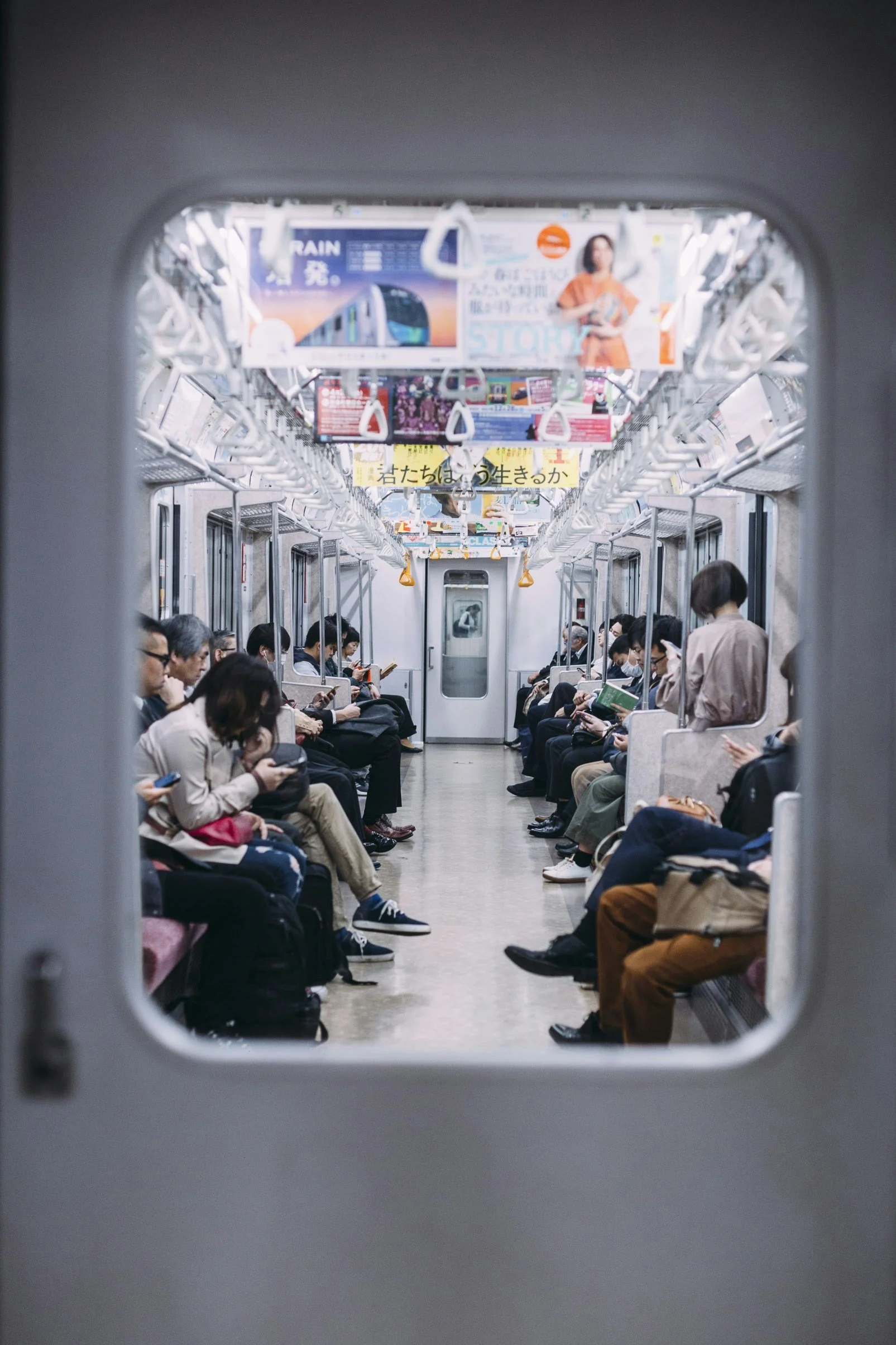 View of a subway train interior with passengers sitting and standing, seen through a train window.