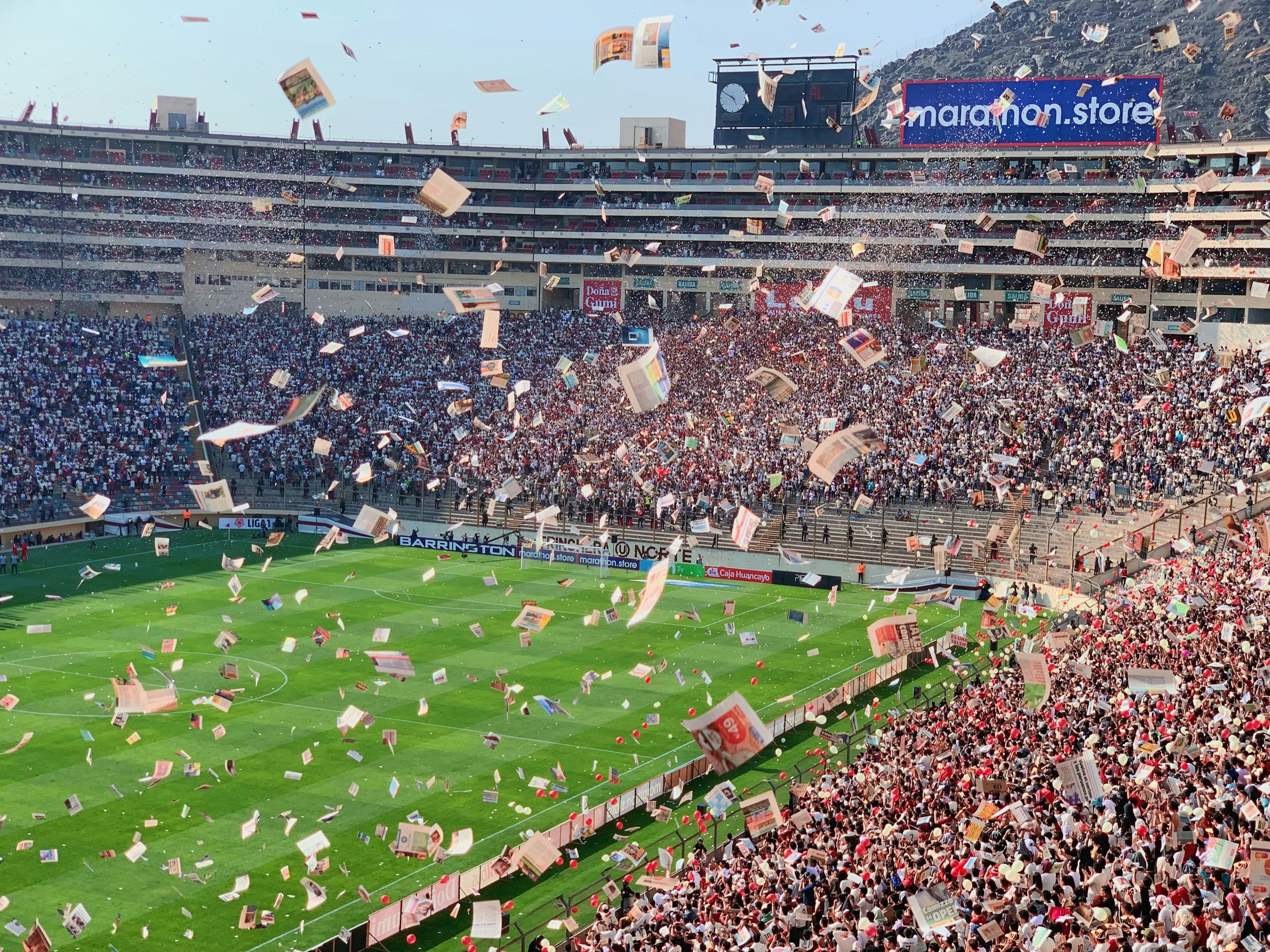 A soccer stadium filled with fans, with confetti and paper debris falling through the air, during a game.