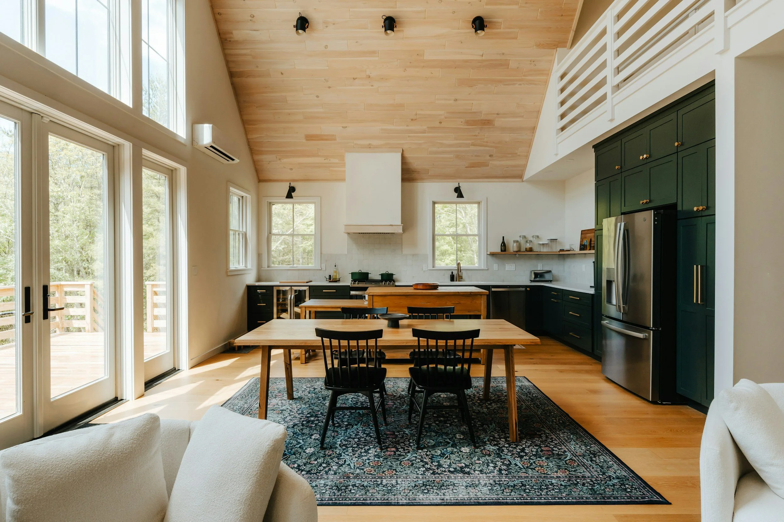 Open-concept kitchen and dining area with natural light, green cabinets, black chairs, wooden dining table, and hardwood floors.