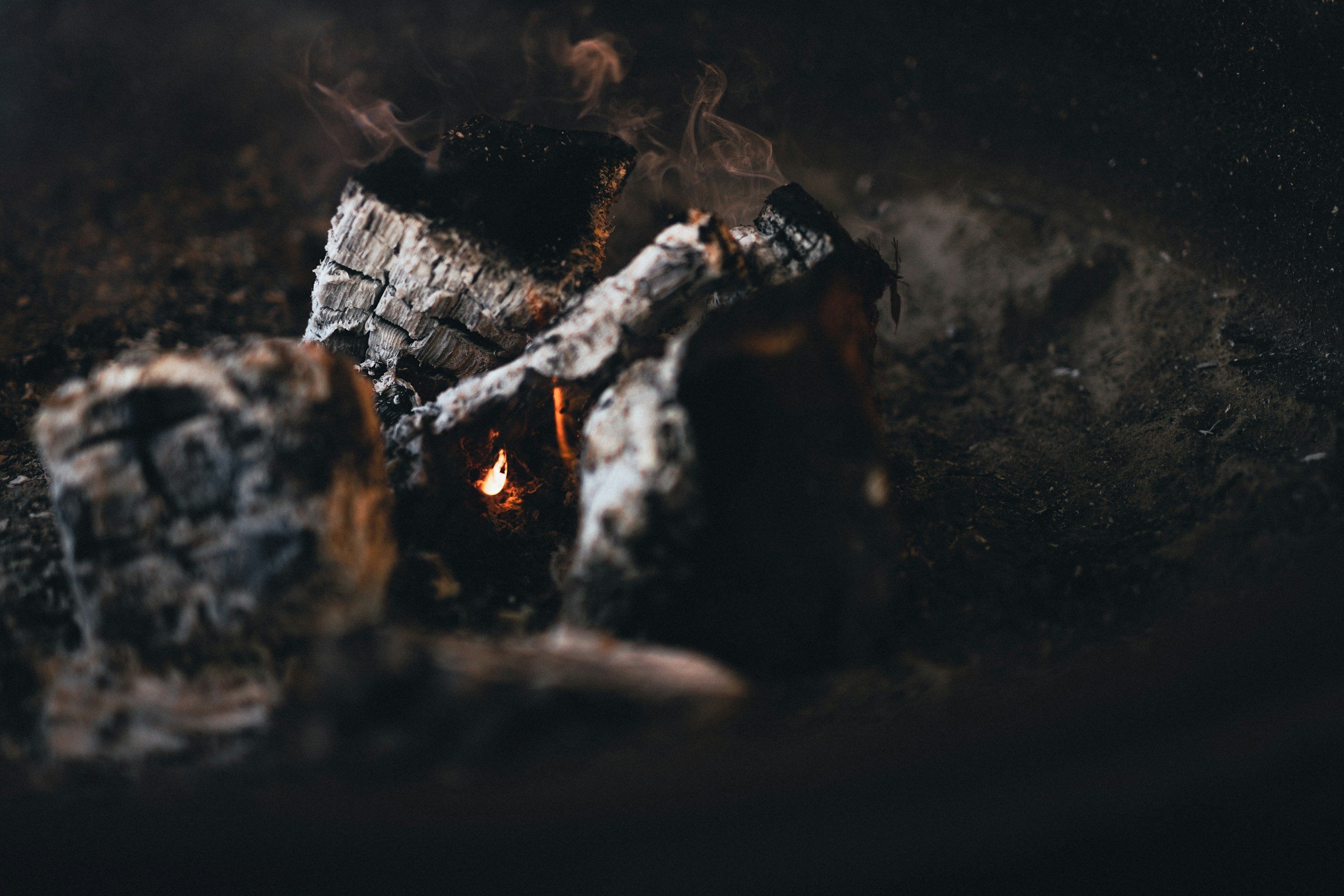 Burning logs on dark ground with visible flames and smoke
