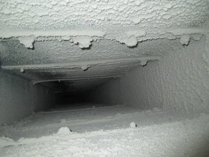 A view inside a cold, icy duct or vent with frost-covered inner surfaces and a dark opening at the far end.