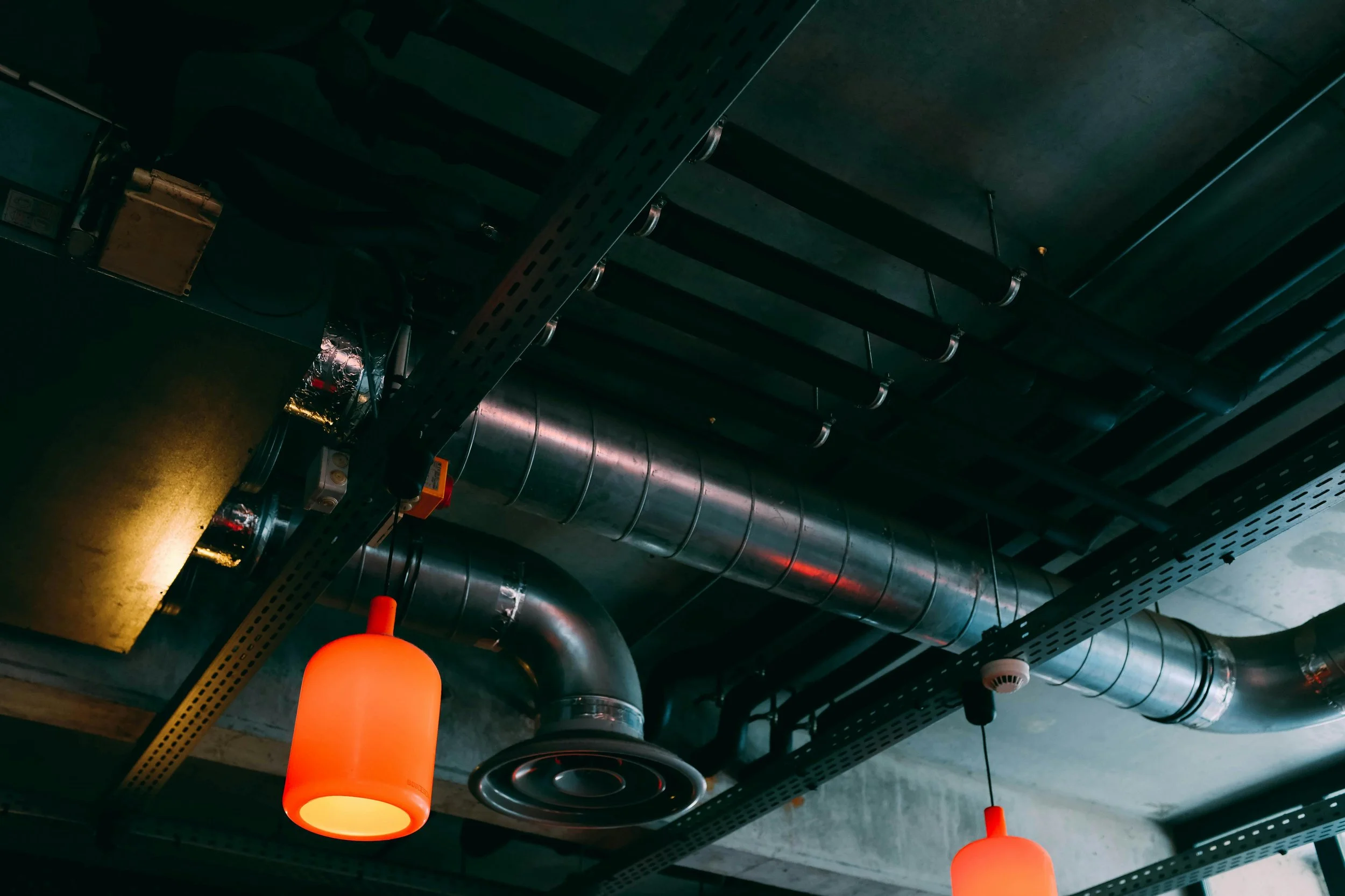 Ceiling with industrial-style black metal beams, exposed silver ductwork, and three glowing orange pendant lights.