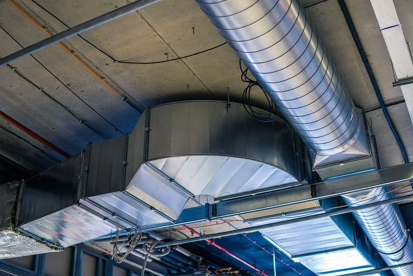 View of industrial air ventilation system with large metallic ducts in an unfinished building ceiling.