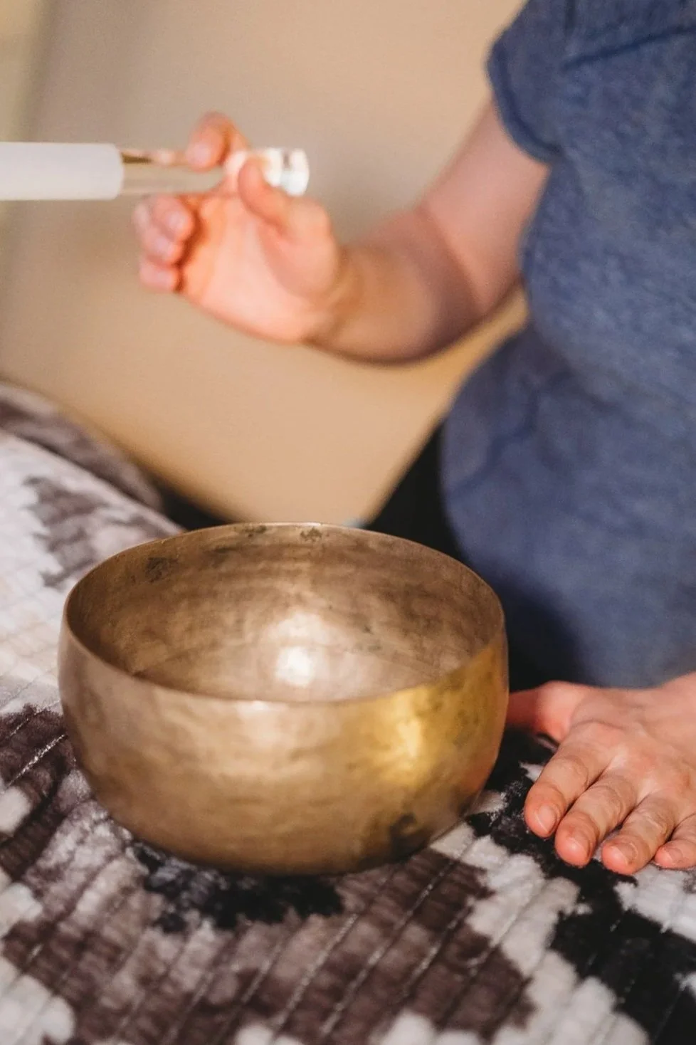 Brass singing bowls with mallet and tingsha cymbals on colorful fabric, glass vase with dried lavender.