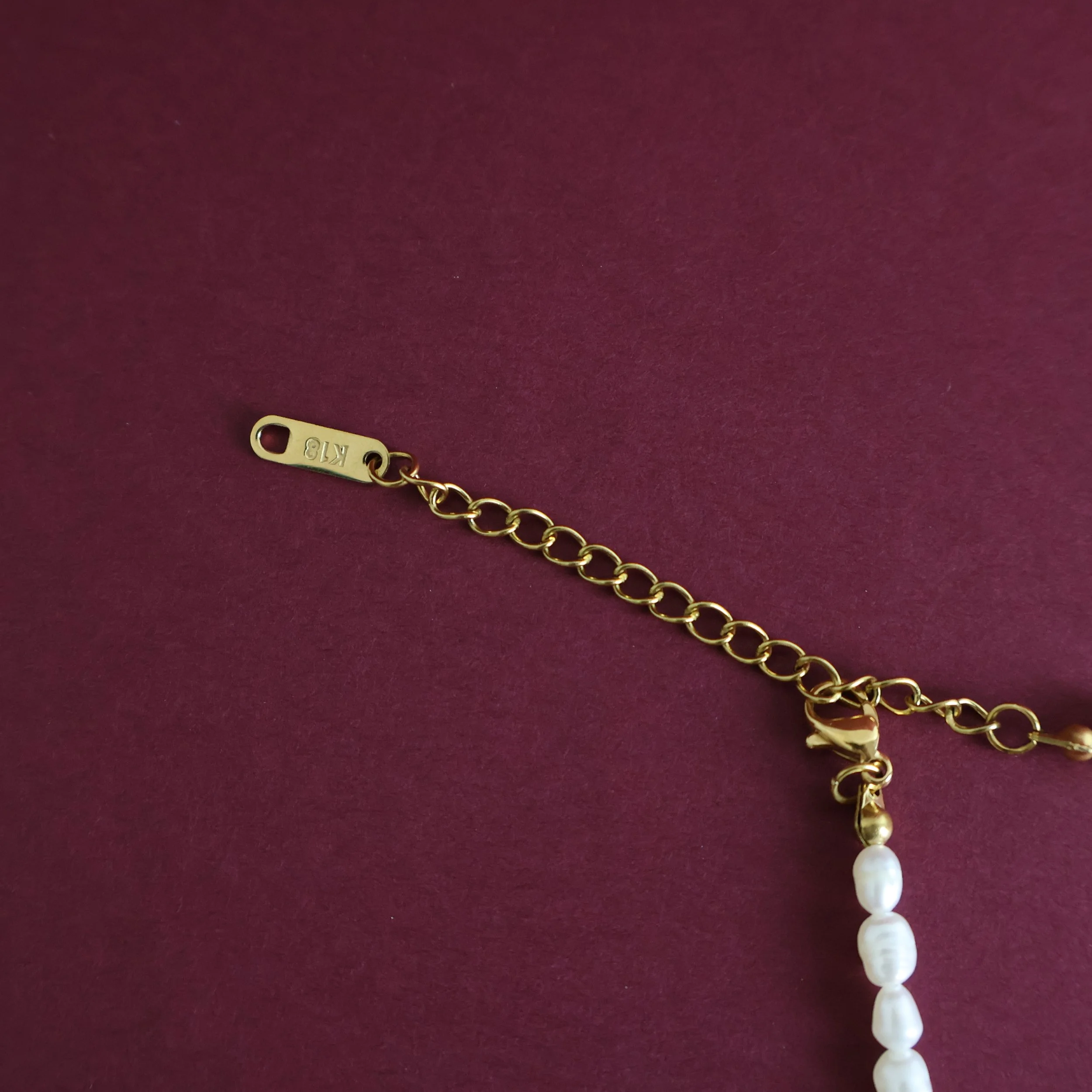 Close-up of the gold-plated lobster clasp and adjustable extension chain on a natural freshwater rice pearl choker necklace.