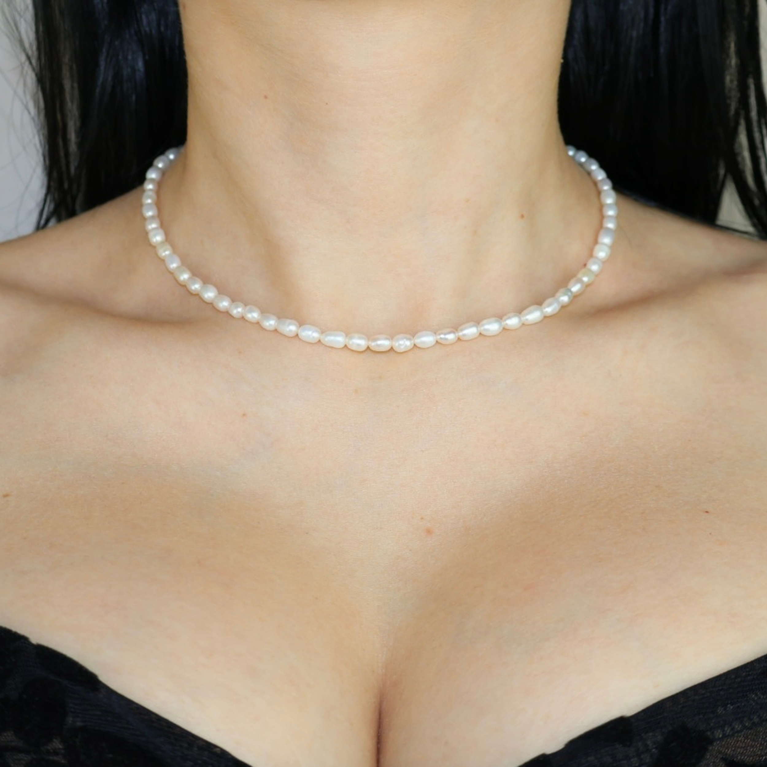 White freshwater rice pearl choker necklace worn around a woman's neck with a black strapless top, showing the delicate minimalist pearl jewellery style.