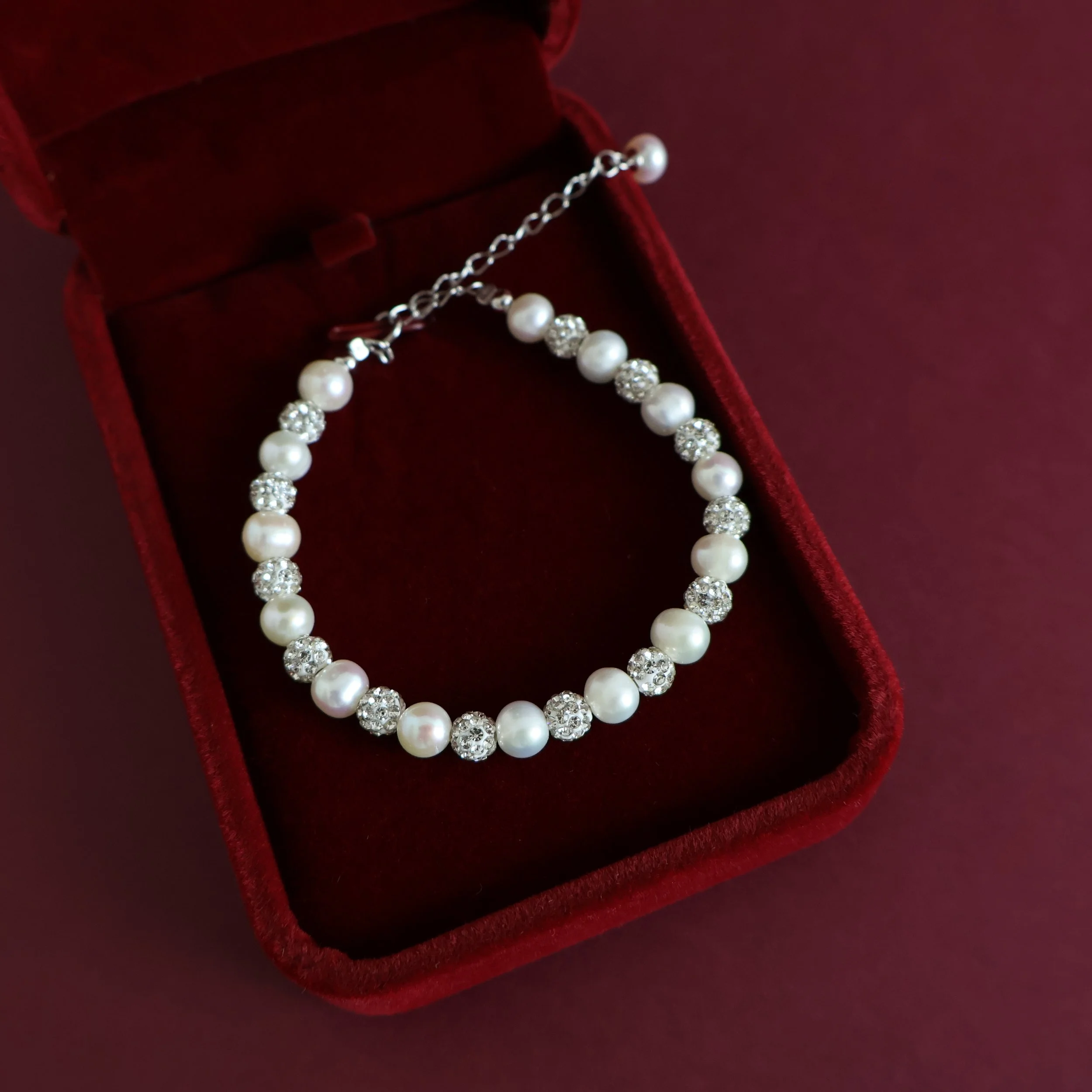 White freshwater pearl and sparkling cubic zirconia bracelet displayed inside an open burgundy jewellery gift box.